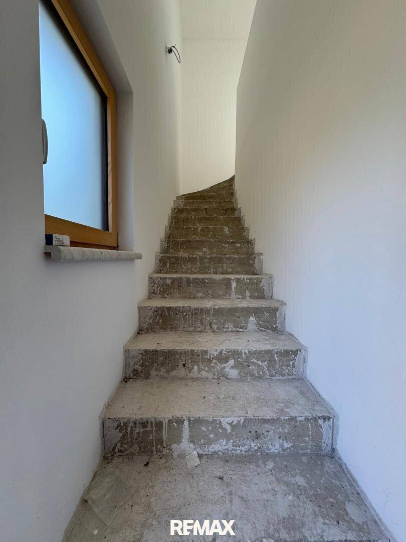 Betontreppe im Rohbau, die in das obere Stockwerk führt, mit Fenster für Tageslicht.