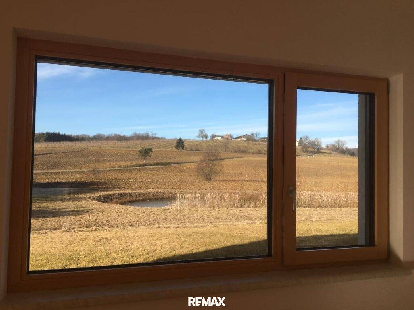 Großes Fenster mit Holzrahmen bietet einen weiten Blick auf Felder und einen Teich.