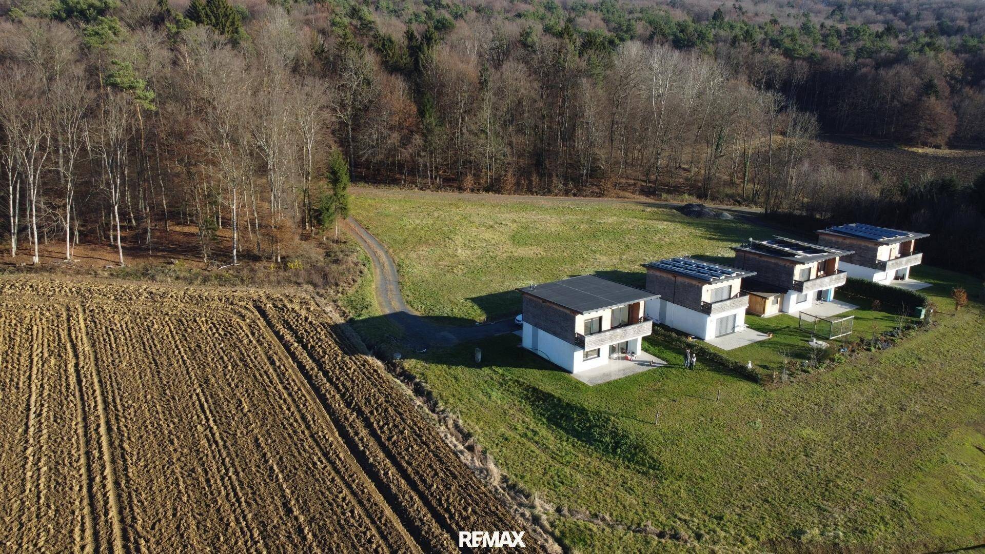 Reihe moderner Einfamilienhäuser mit Holzfassaden und Solaranlagen in ländlicher Umgebung.