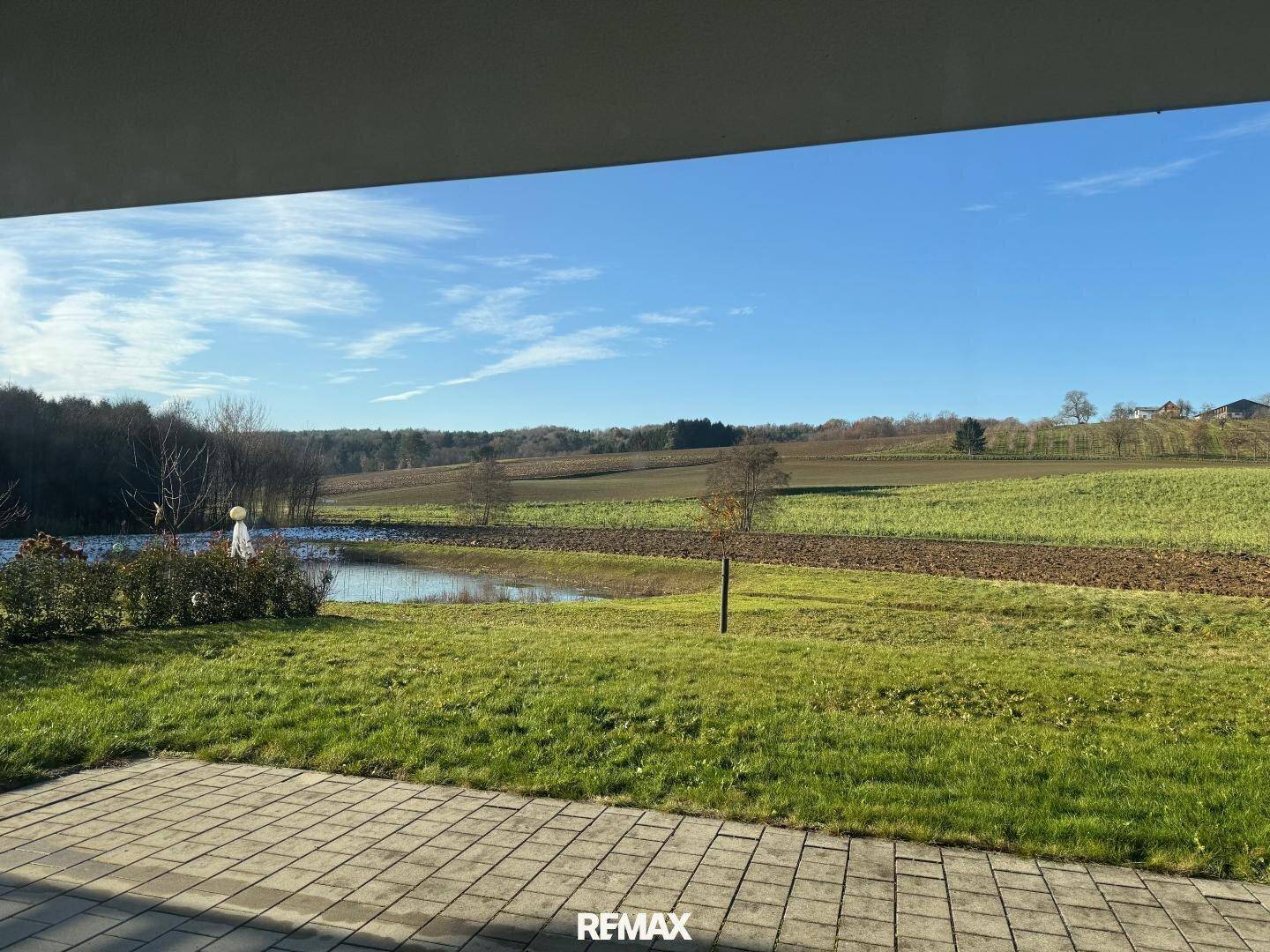 Gepflasterte Terrasse mit weitem Blick über grüne Felder und einen kleinen Teich.