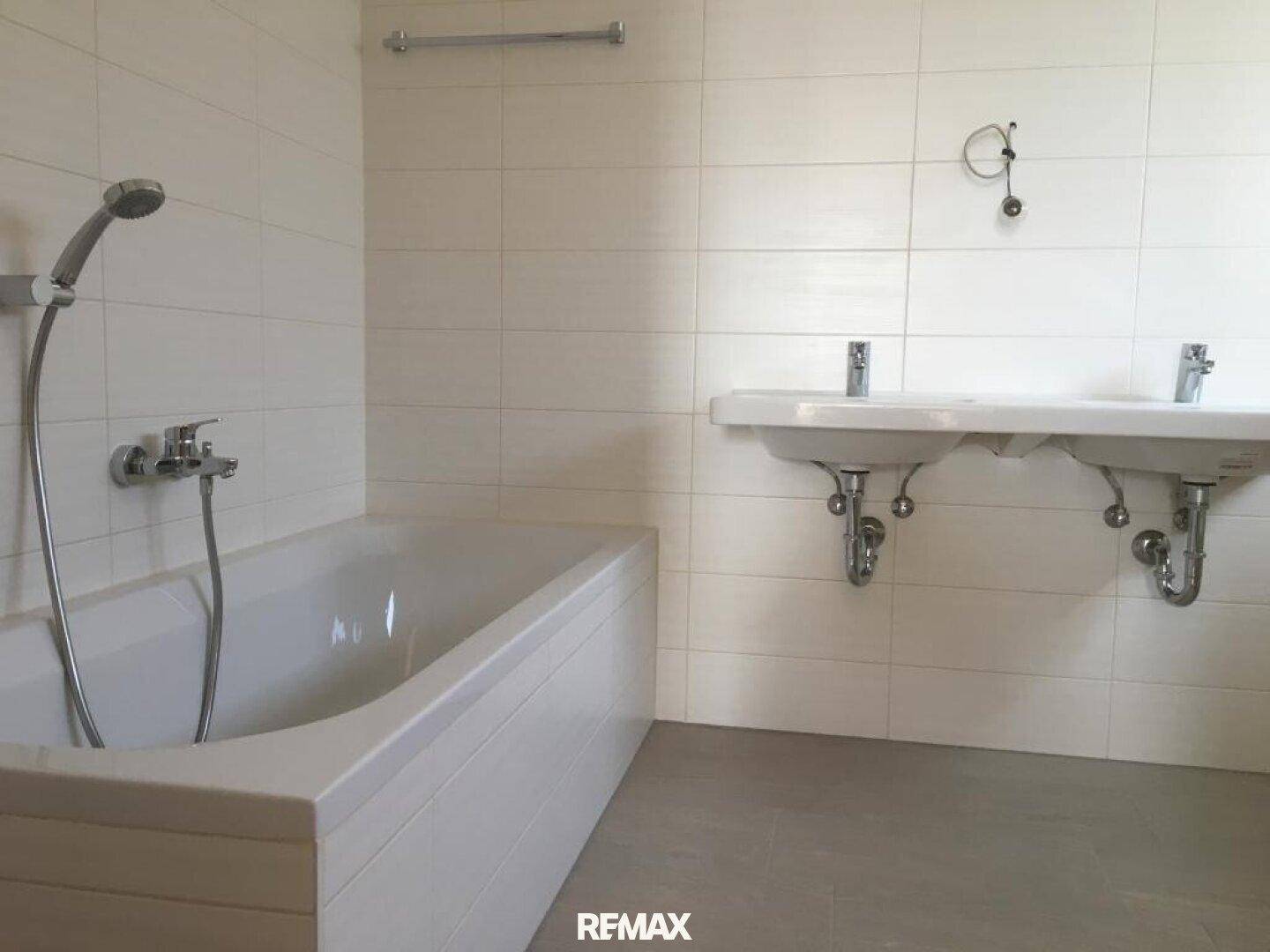 Modern gefliestes Badezimmer mit Badewanne und zwei Waschbecken, in gutem Zustand.