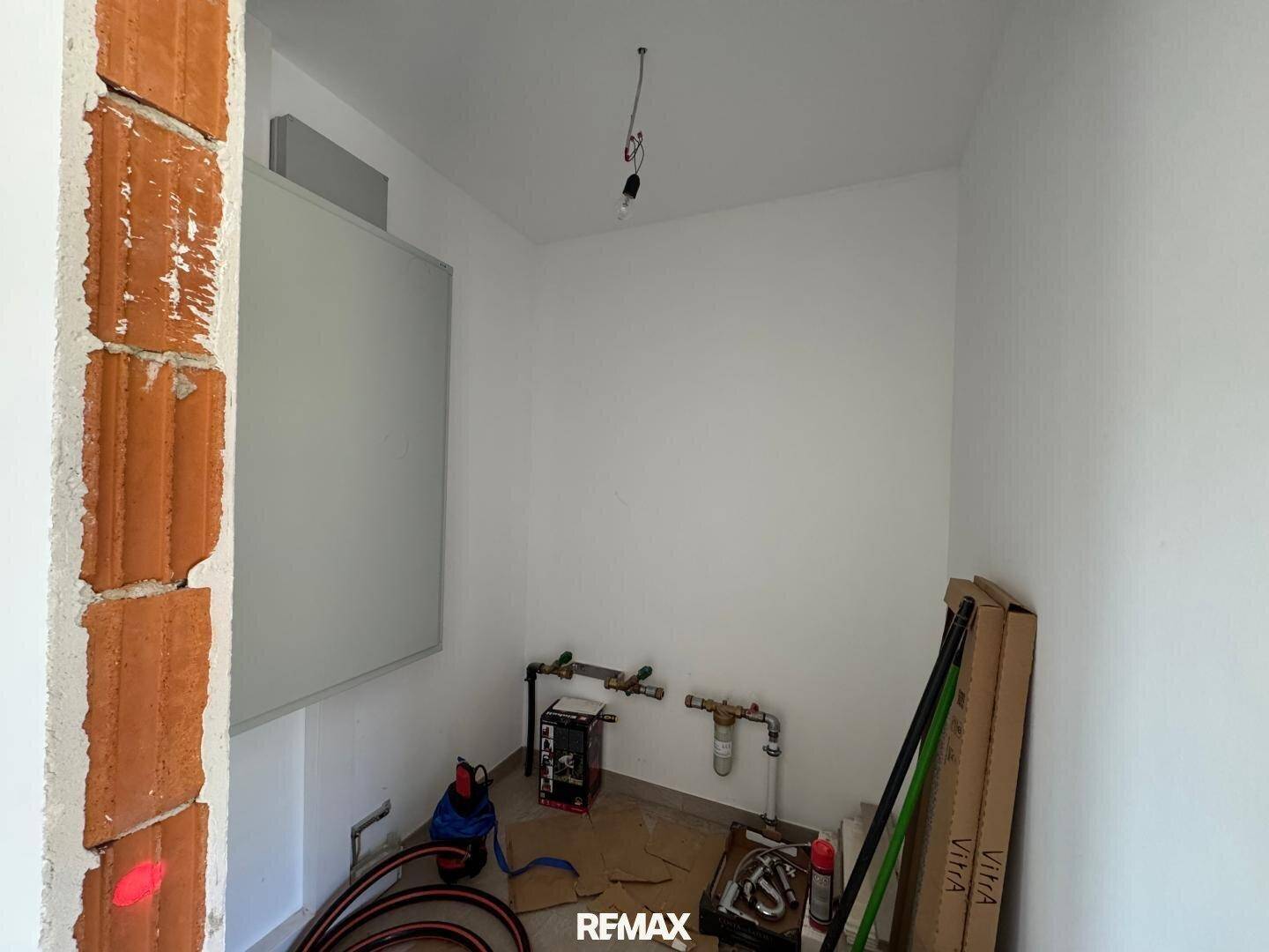 Unfertiger Technikraum mit sichtbaren Installationen und weiß gestrichenen Wänden.
