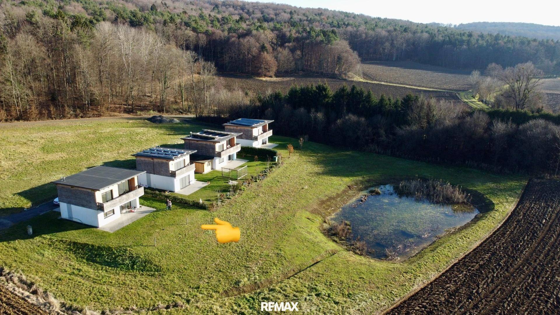 Luftaufnahme einer Siedlung moderner Häuser mit Teich und angrenzenden Feldern und Wald.