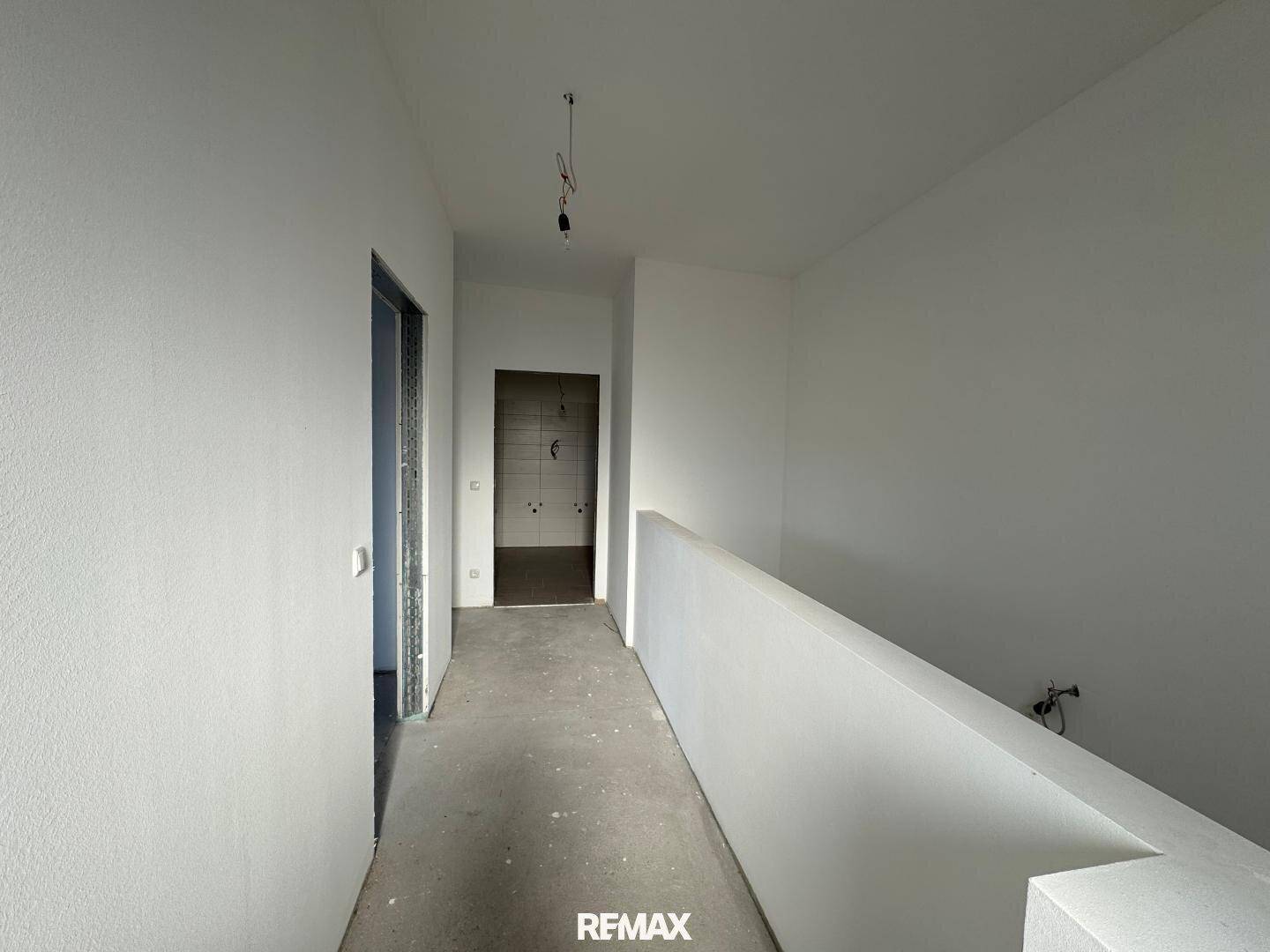 Heller Flur im Obergeschoss im Rohbau mit Betonboden und Zugang zu weiteren Räumen.