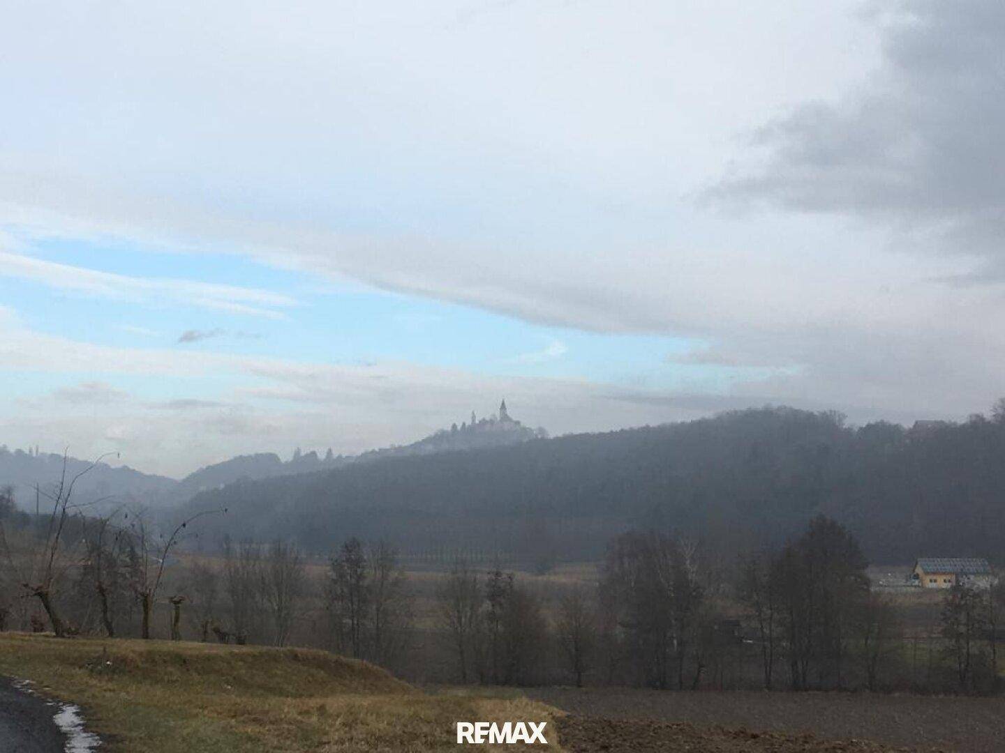 Weitläufige Hügellandschaft mit einem Dorf auf einem Berg im Nebel.