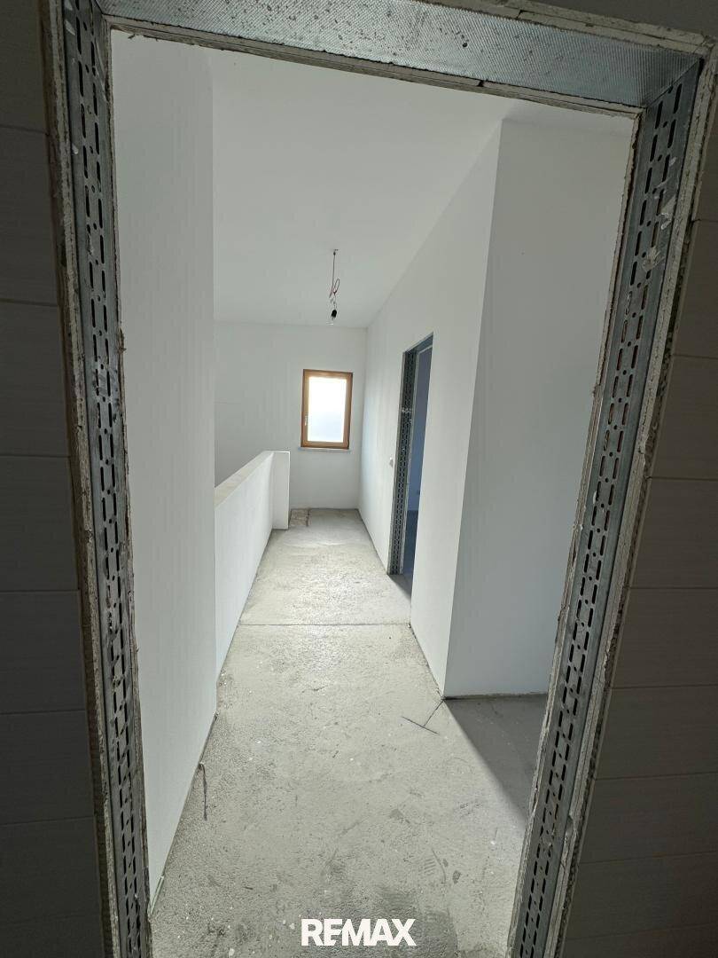Langer Flur im Obergeschoss im Rohbau mit Fenster und Zugang zu den Zimmern.