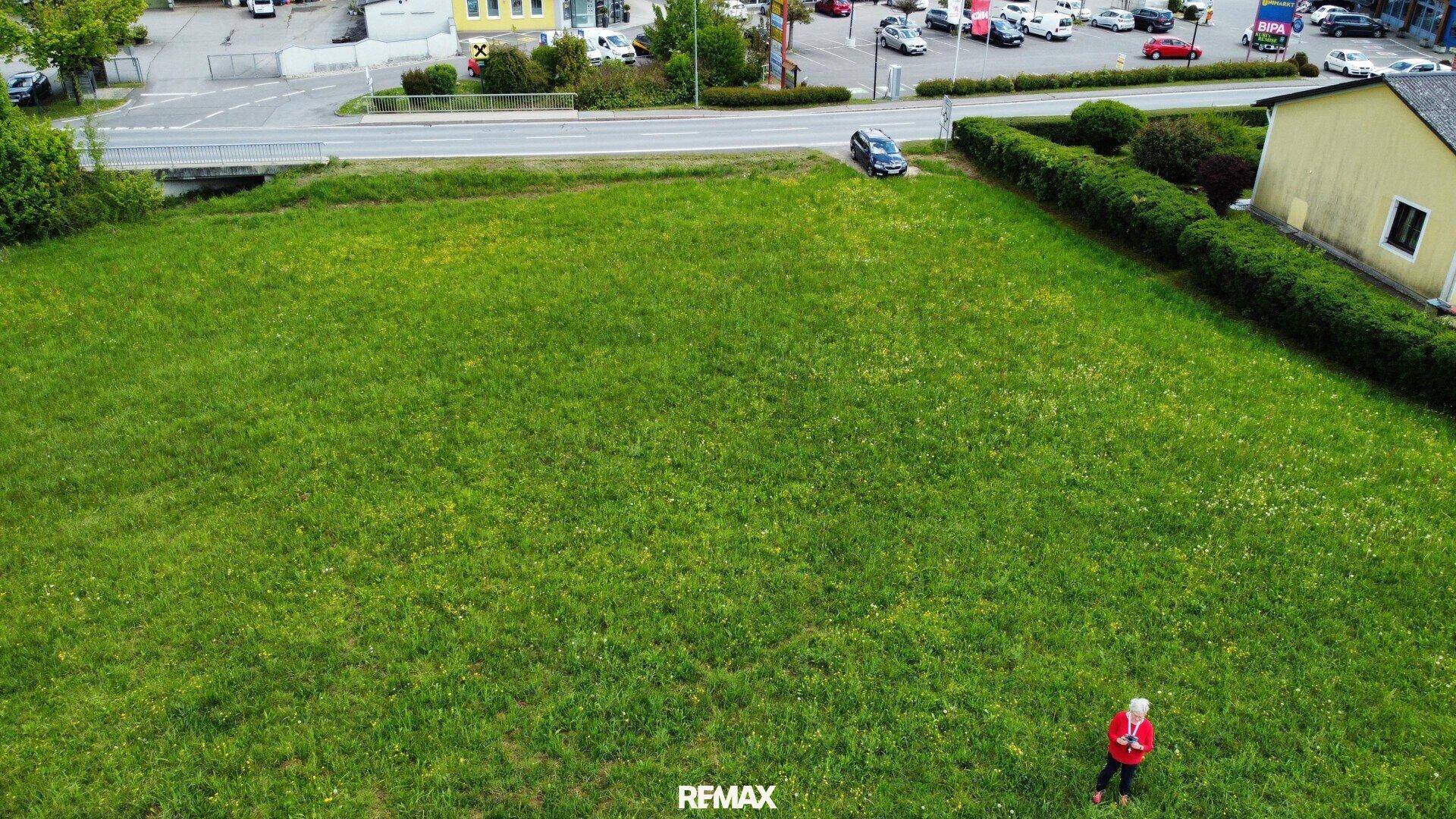 Luftaufnahme eines großen grünen Grundstücks neben einer Straße mit Gewerbe und einer Person.