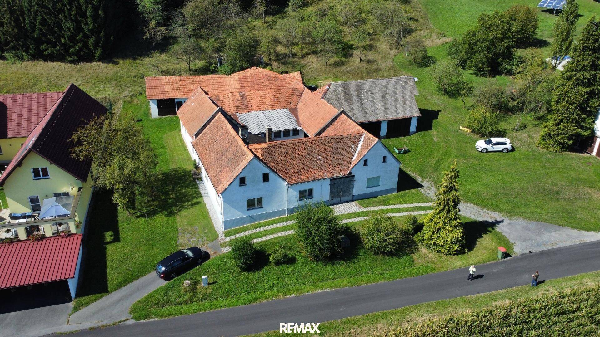 Weitläufige Luftaufnahme eines Bauernhofs mit angrenzenden Feldern und Waldgebieten unter blauem Himmel.