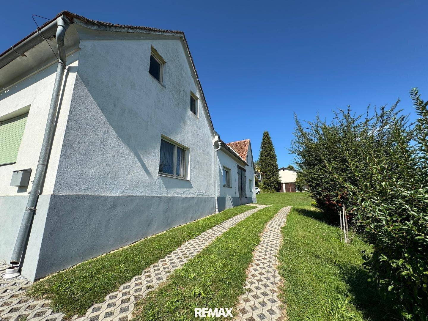 Seitenansicht eines Landhauses mit weißer Fassade, grauer Basis und gepflasterter Auffahrt.