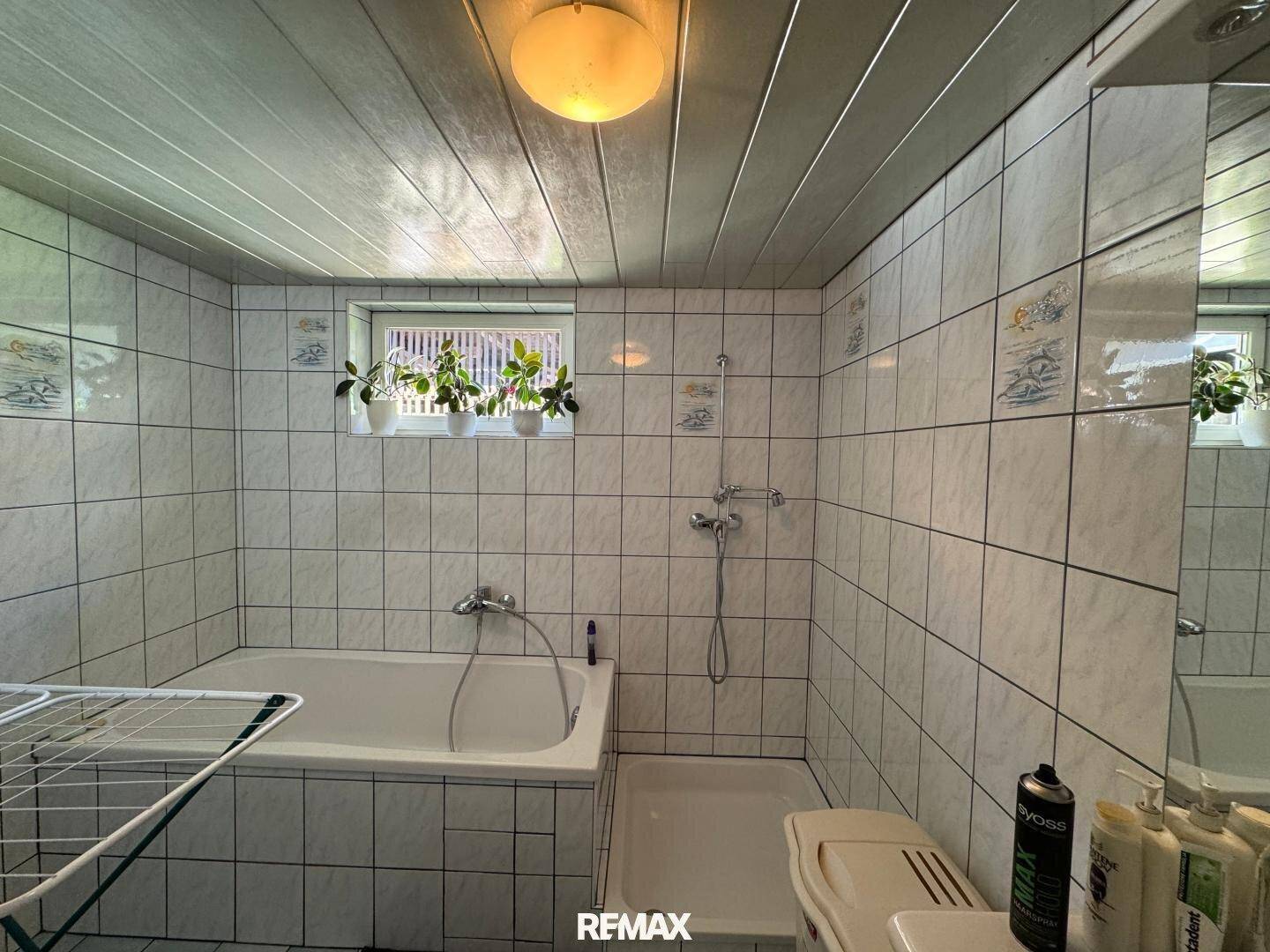 Gefliestes Badezimmer mit Badewanne, Duscharmatur und einem Fenster für Tageslicht.