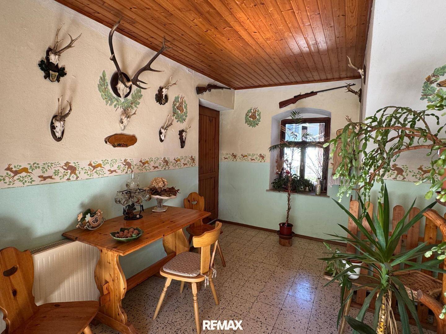 Rustikaler Essbereich mit Holztisch, Stühlen und traditionellen Jagdtrophäen an der Wand.