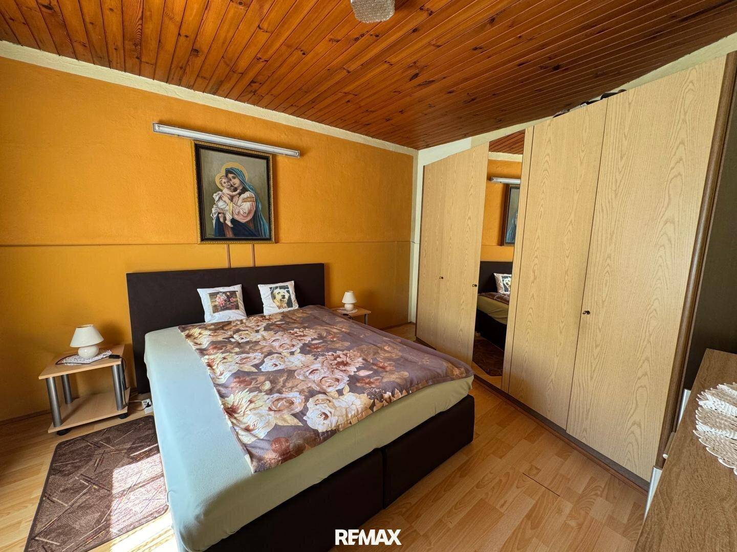 Schlafzimmer mit orangefarbenen Wänden, Doppelbett und Einbauschränken mit Spiegeltüren.