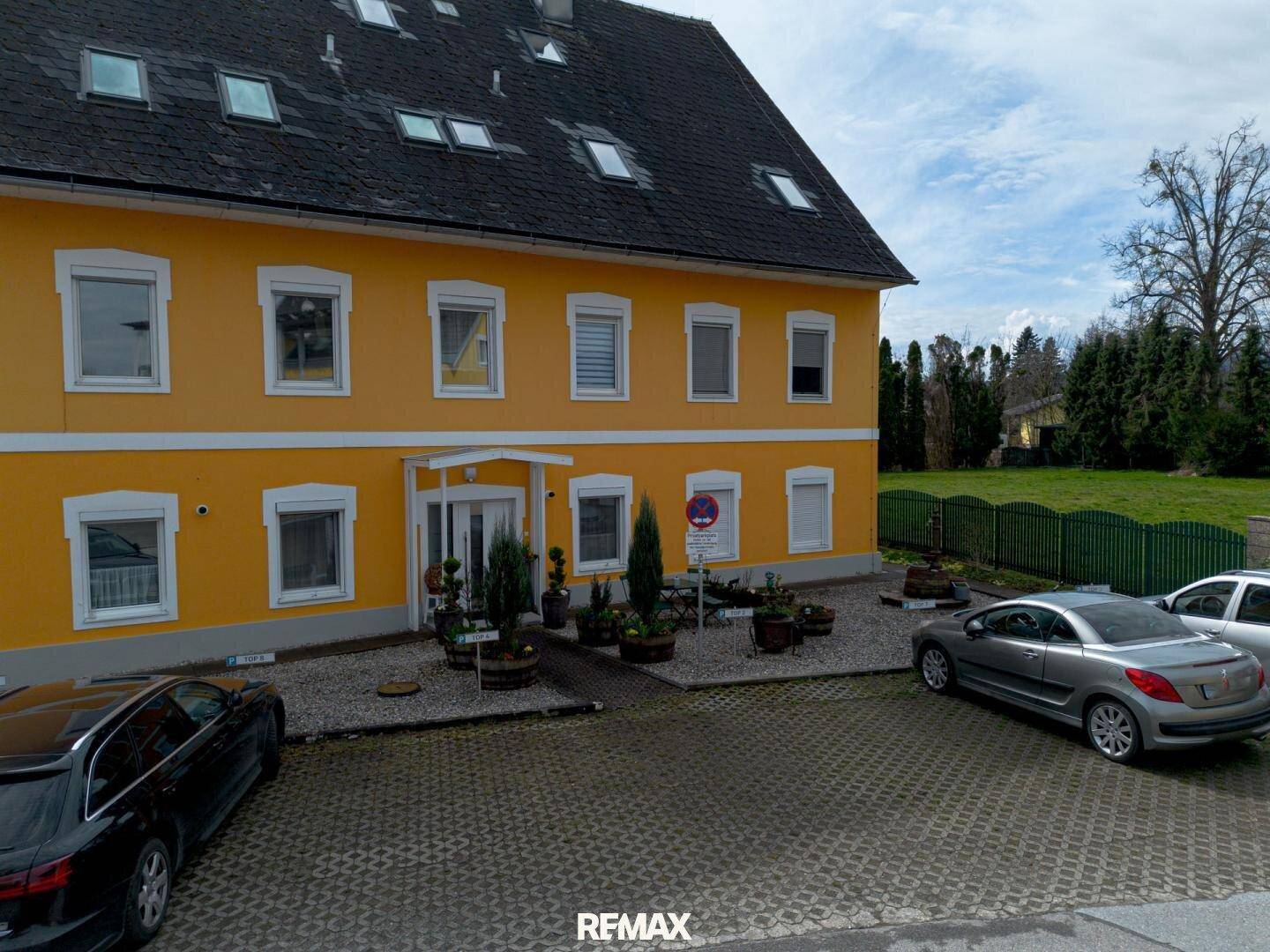 Ansicht der gelben Fassade des Gebäudes mit weißen Fenstern und gepflegtem Eingangsbereich.