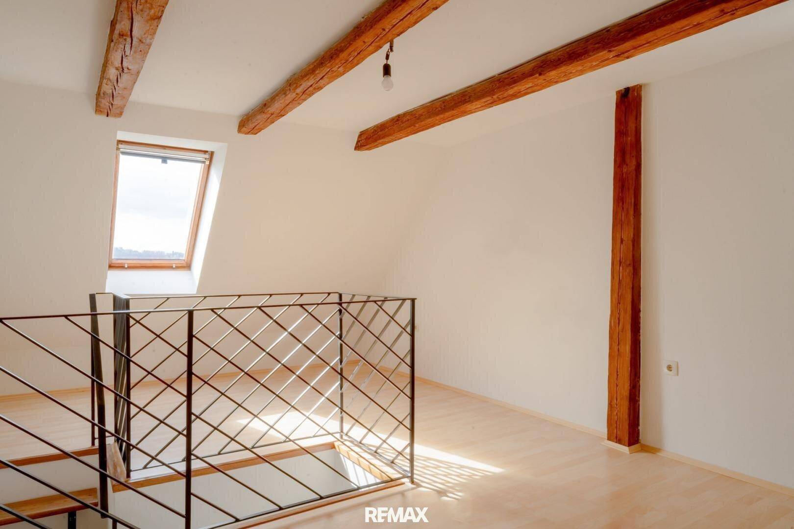 Lichtdurchfluteter Dachraum mit freiliegenden Holzbalken, Dachfenster und offener Treppe.