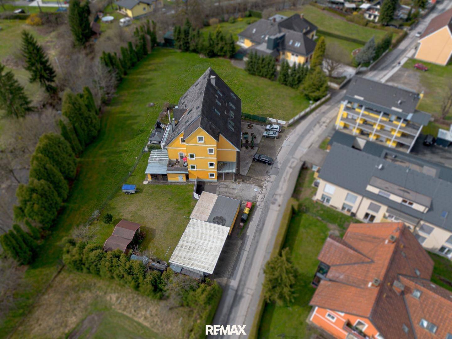 Vogelperspektive des gelben Hauses mit Carport und weitläufiger Grünfläche in ländlicher Umgebung.