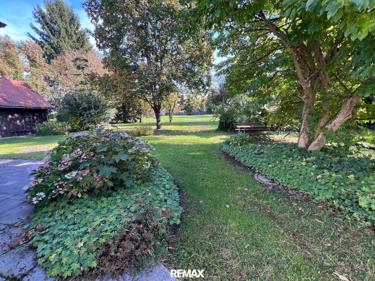 Idyllischer Gartenbereich mit Sitzgelegenheiten unter Bäumen und üppiger Bepflanzung.