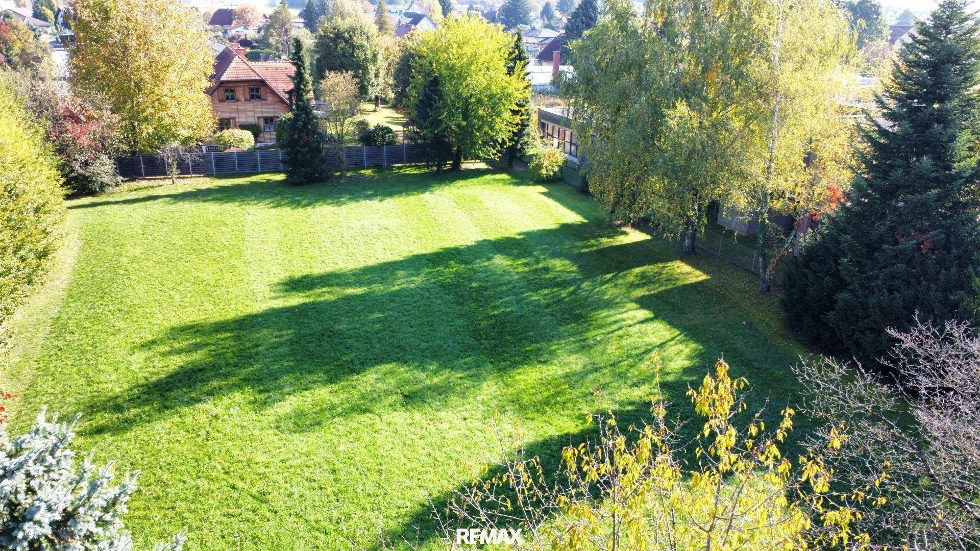 Weitläufiger grüner Garten mit gepflegtem Rasen und Schattenwurf von Bäumen.