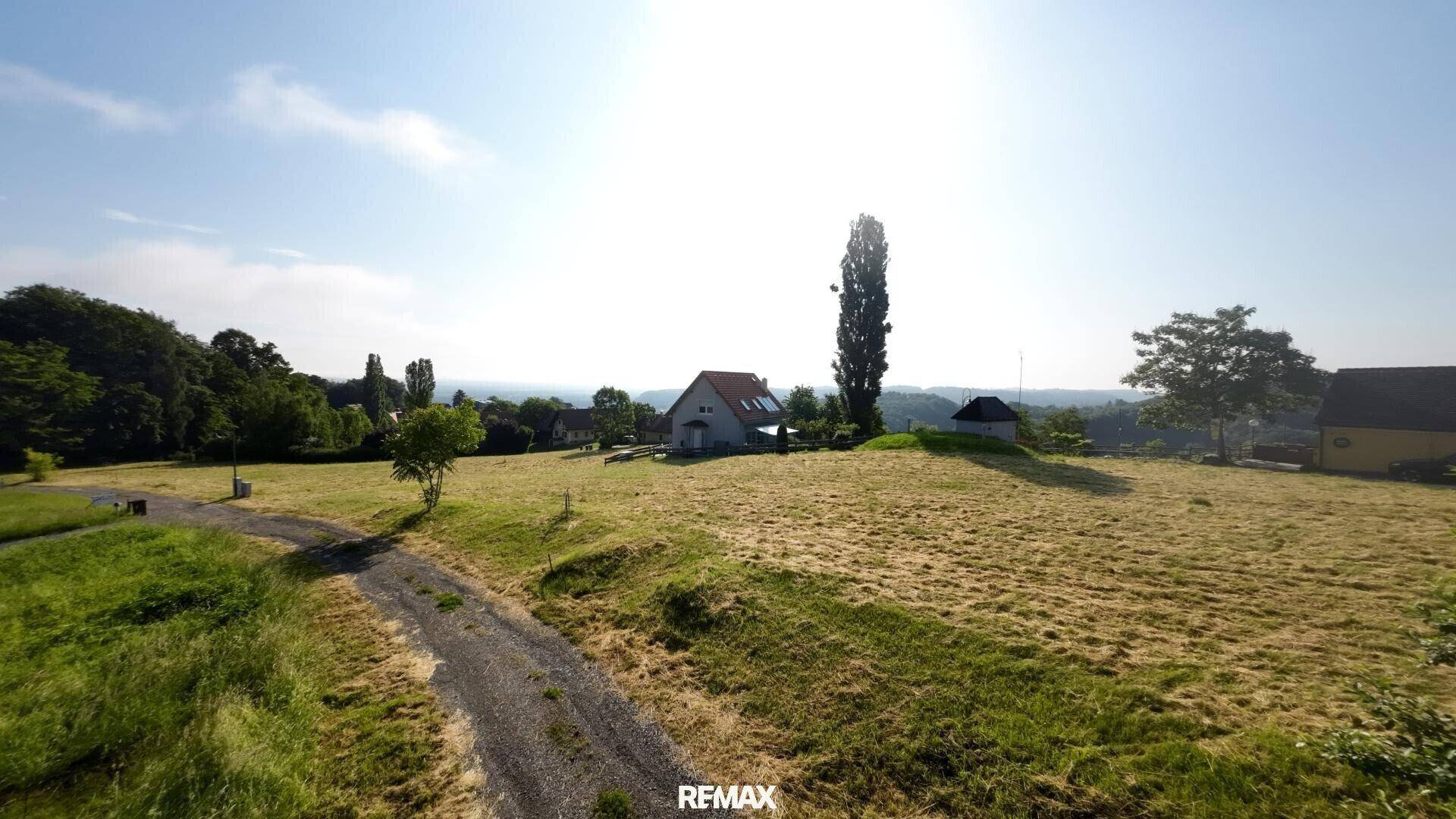 Luftaufnahme einer weiten Feldlandschaft mit einem einzelnen Haus und Bäumen am Horizont.
