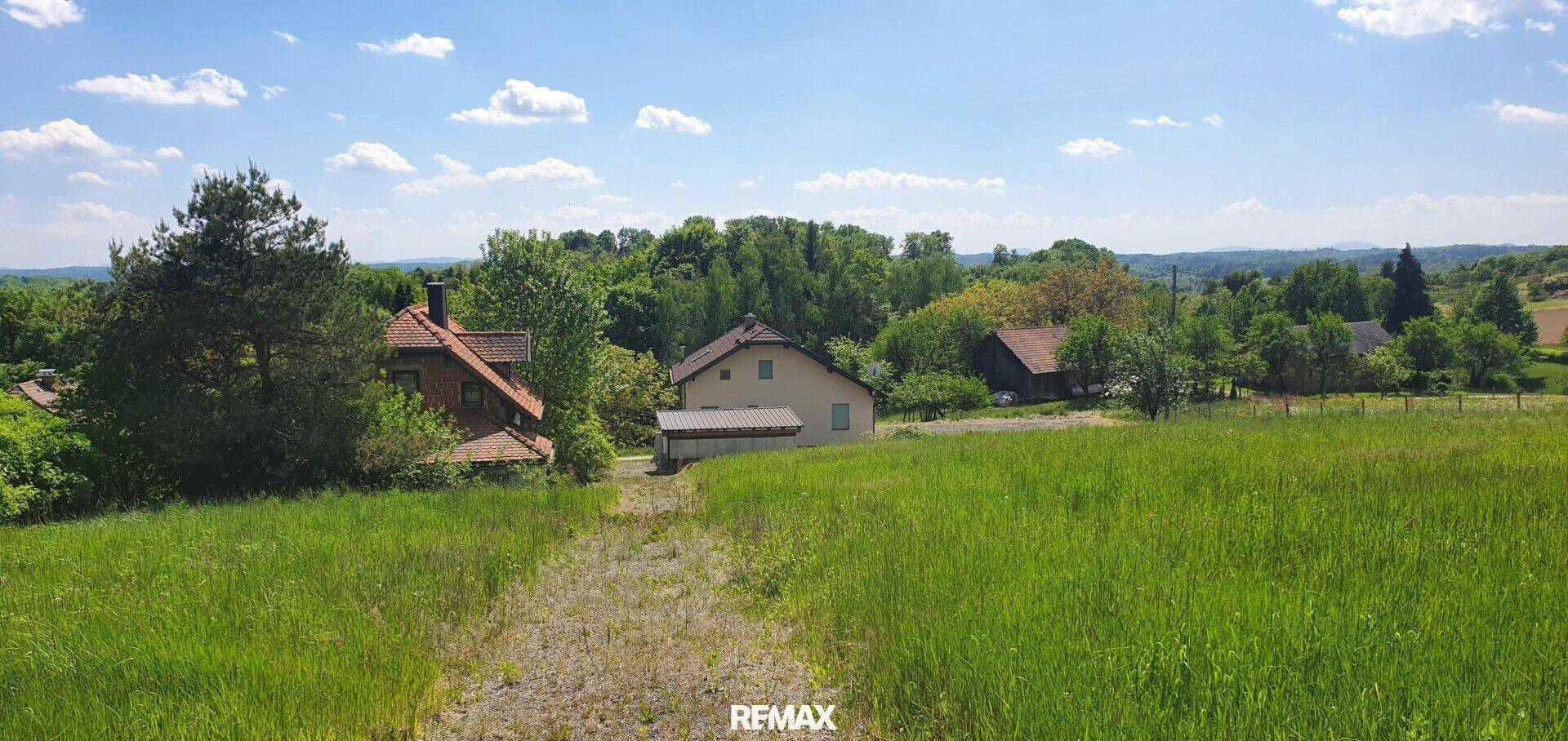 Grünes Grundstück mit Feldweg und Blick auf die umliegende ländliche Bebauung unter blauem Himmel.