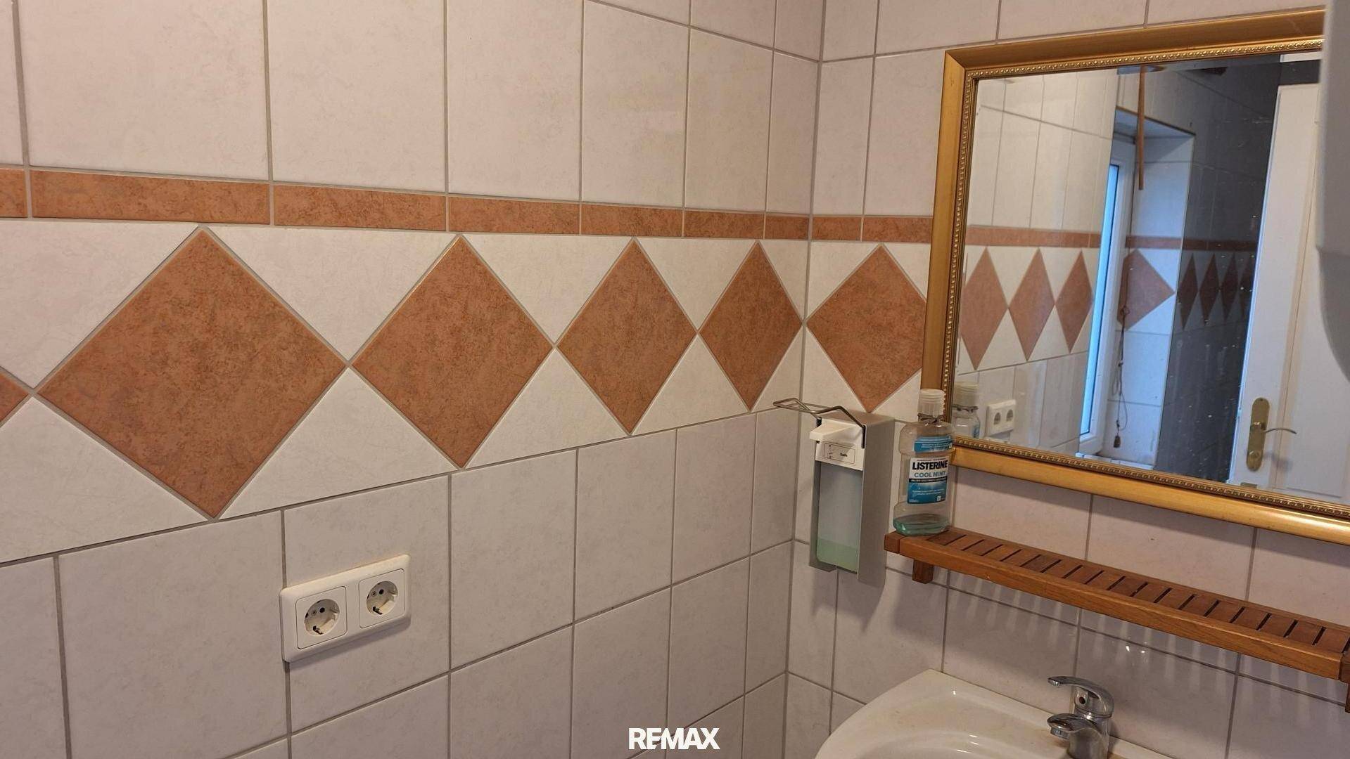 Gefliestes WC mit Spiegel, Waschbecken und gemusterten Wandfliesen in Braun- und Beigetönen.
