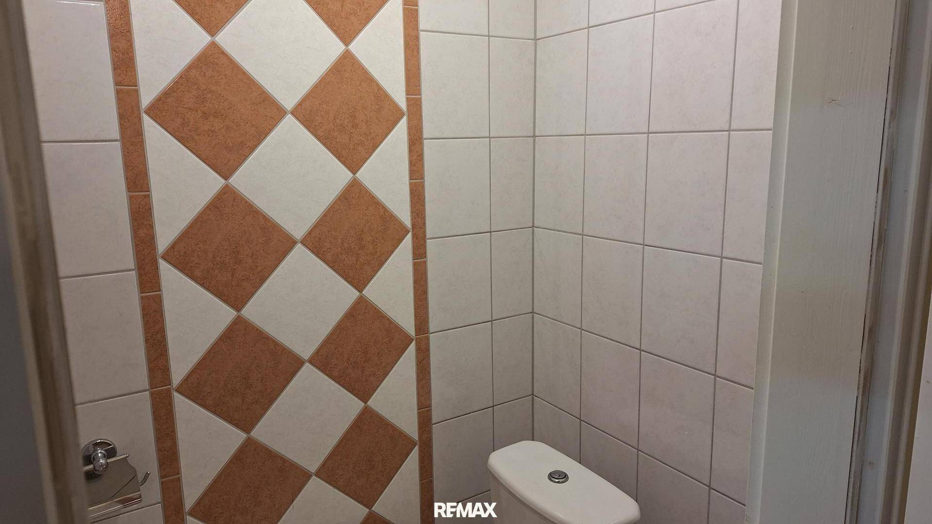 Kleines WC mit Steh-WC und gemusterten Wandfliesen in Braun- und Beigetönen.