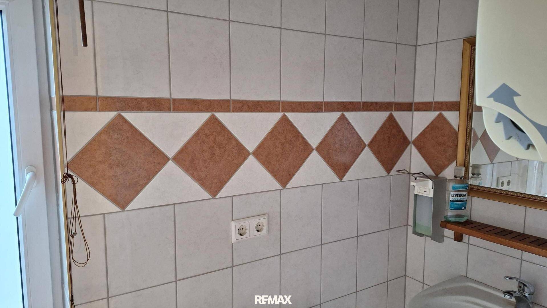 Gefliestes WC mit Spiegel, Waschbecken und gemusterten Wandfliesen in Braun- und Beigetönen.