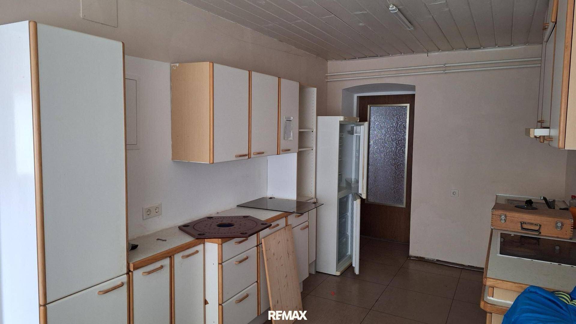 Ältere Einbauküche mit weißen und holzfarbenen Schränken, Kühlschrank und Fliesenboden.