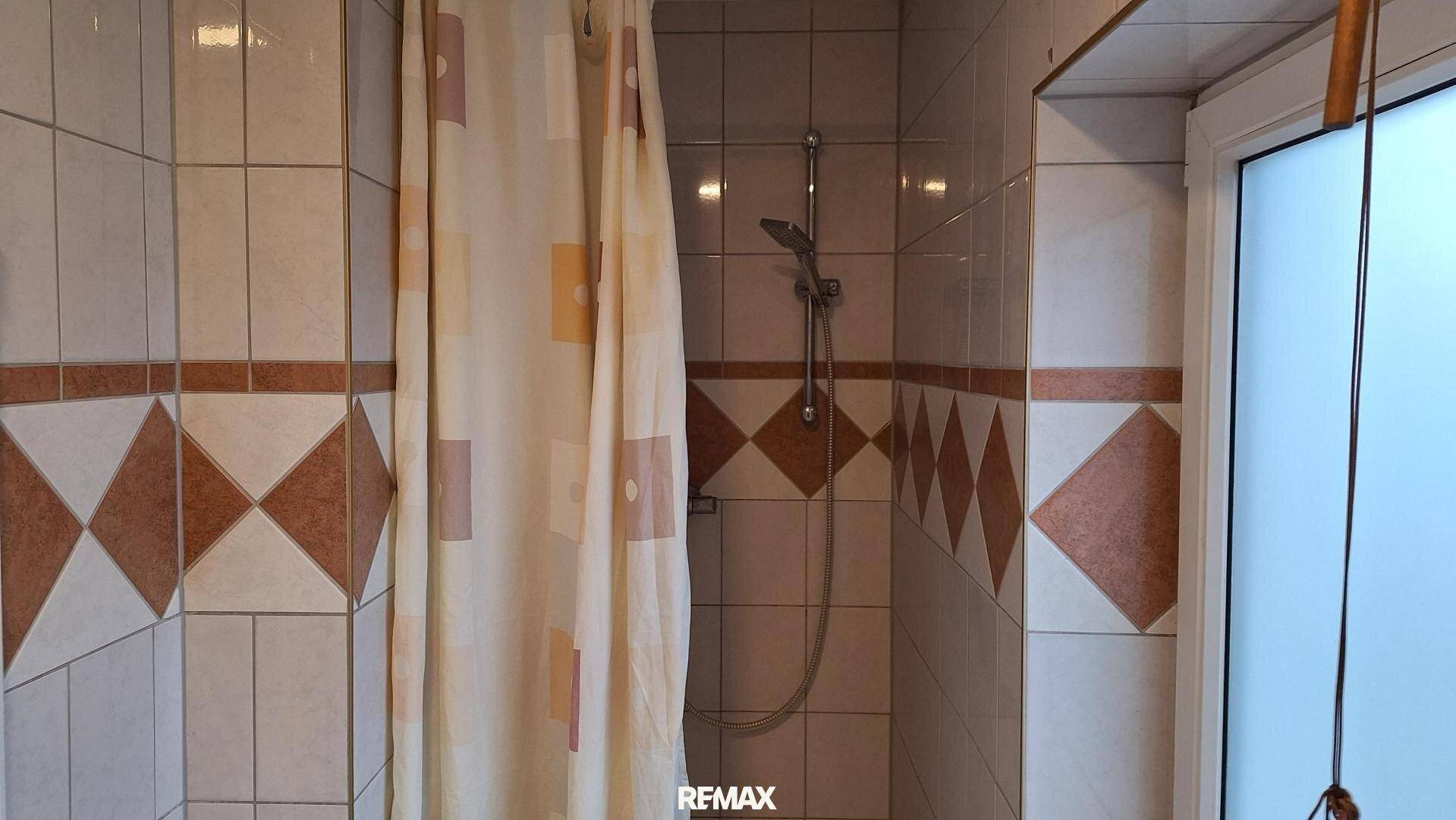 Badezimmer mit Duschbereich und gemusterten Wandfliesen in Braun- und Beigetönen.