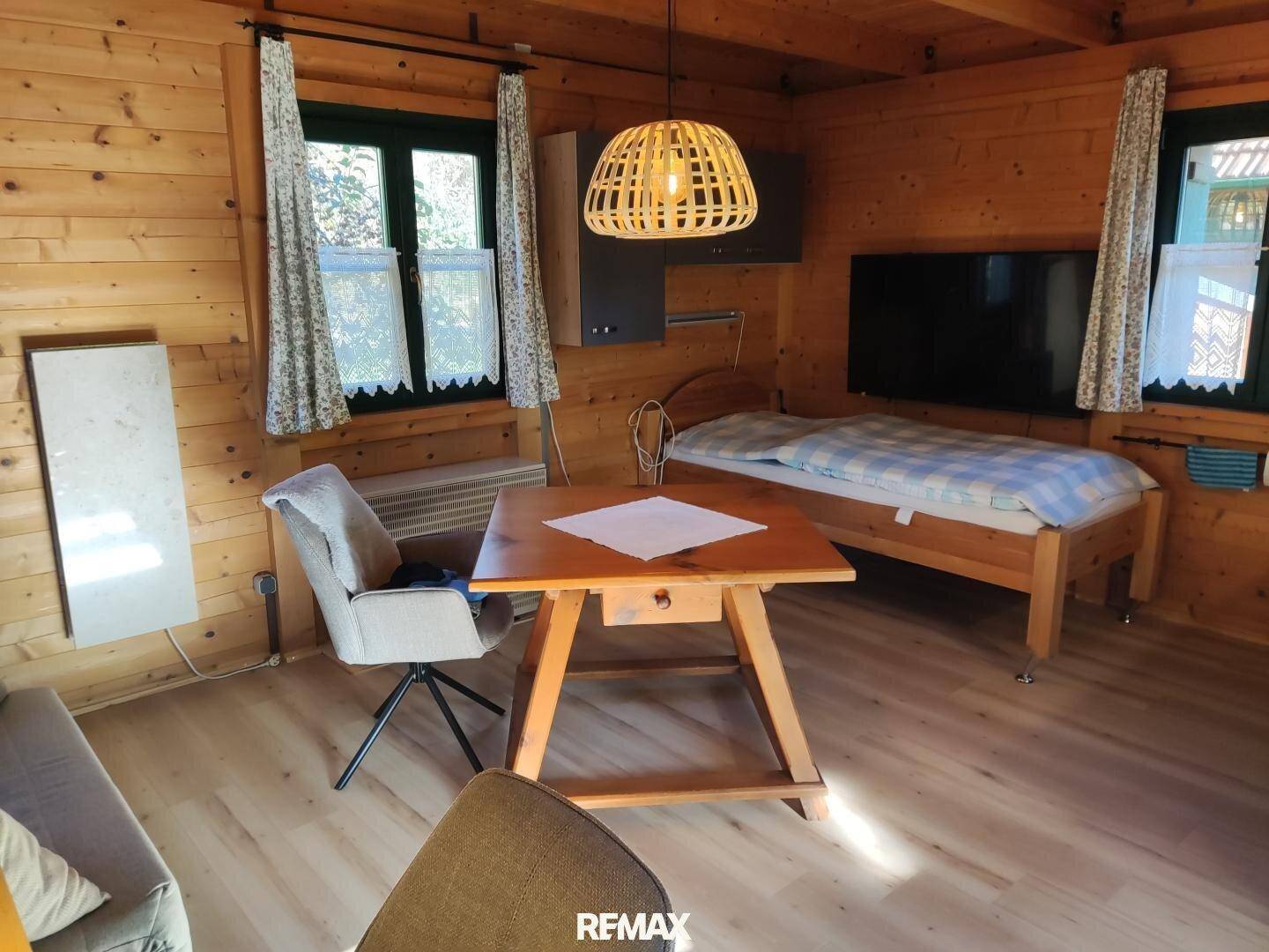 Schlafzimmer mit Holzwänden, Einzelbett, Esstisch und moderner Hängelampe in warmem Licht.