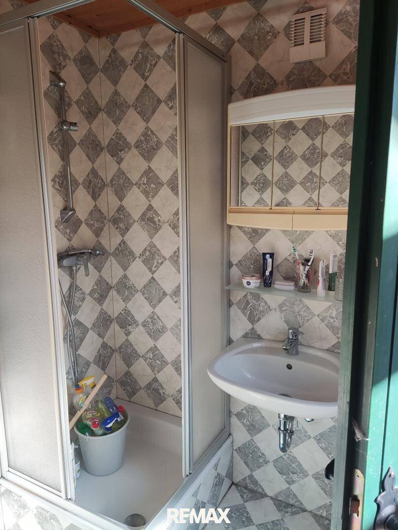 Kleines Badezimmer mit Duschkabine, Waschbecken und gemusterten Fliesen in hellem Licht.