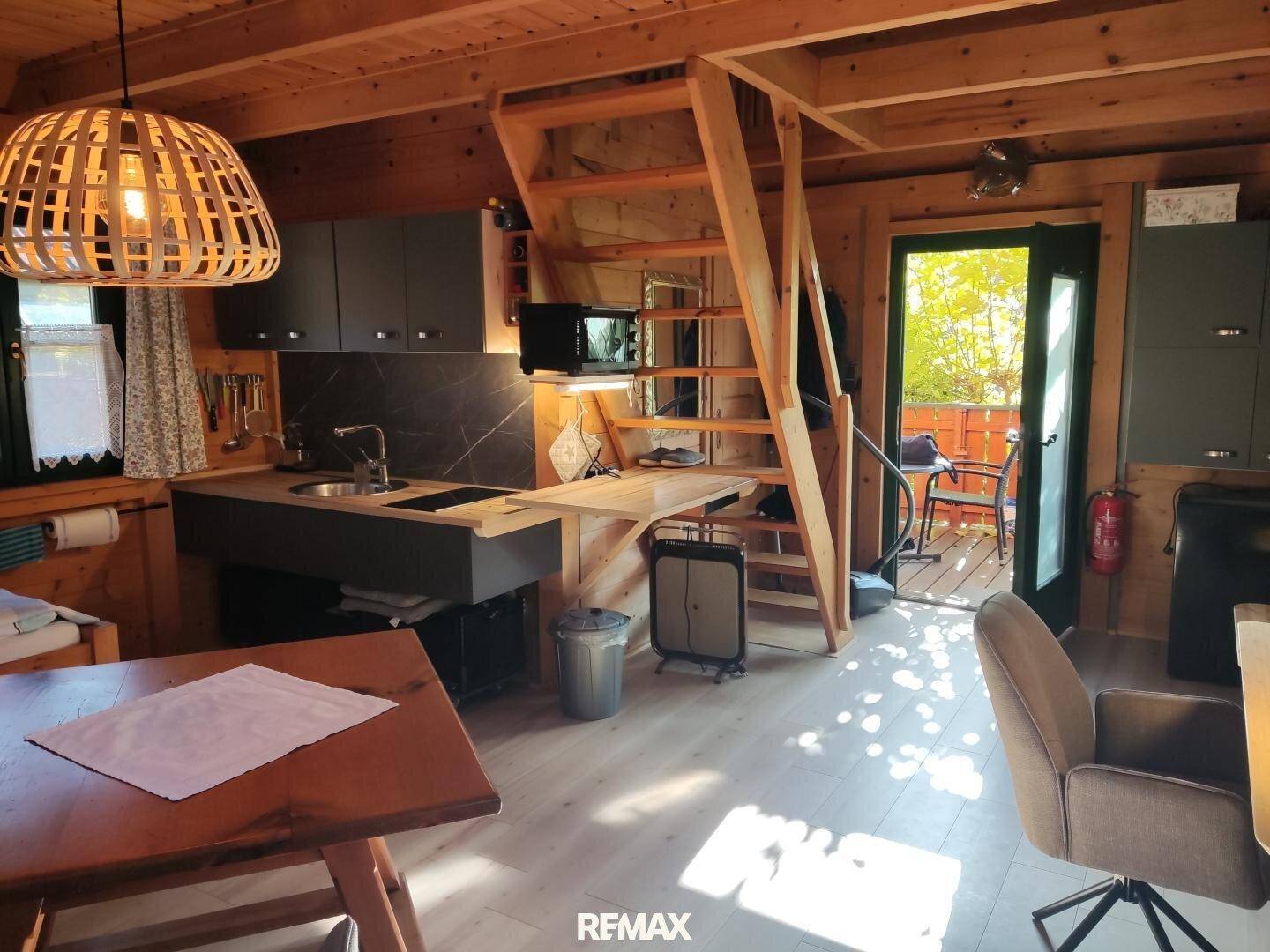 Offener Wohnbereich mit kleiner Küche, Esstisch und Zugang zum Balkon in rustikalem Stil.