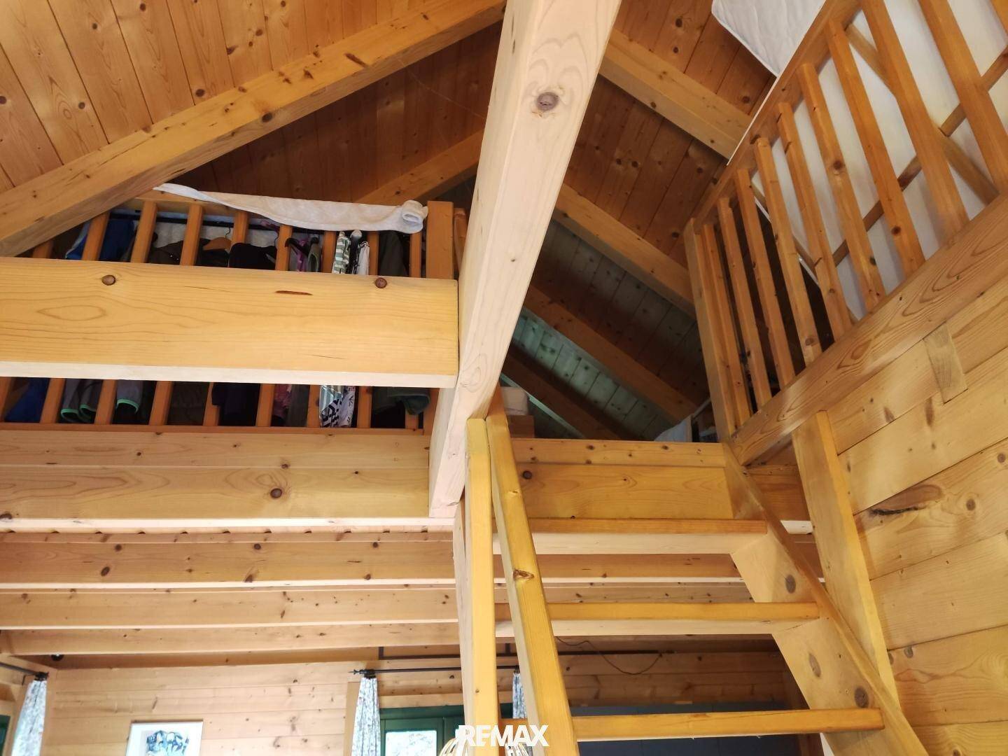 Rustikaler Dachbodenbereich mit sichtbaren Holzbalken und einer Holztreppe, die zum Schlafbereich führt.