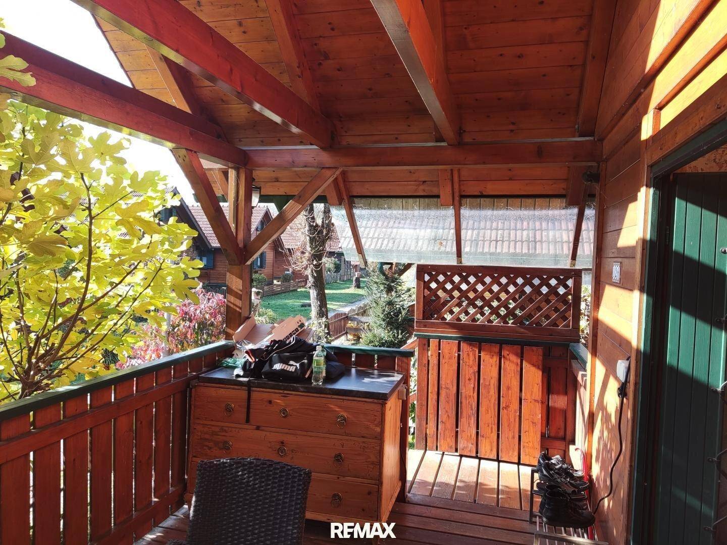 Überdachter Holzbalkon mit Blick ins Grüne und rustikalen Möbeln, ideal zum Entspannen.