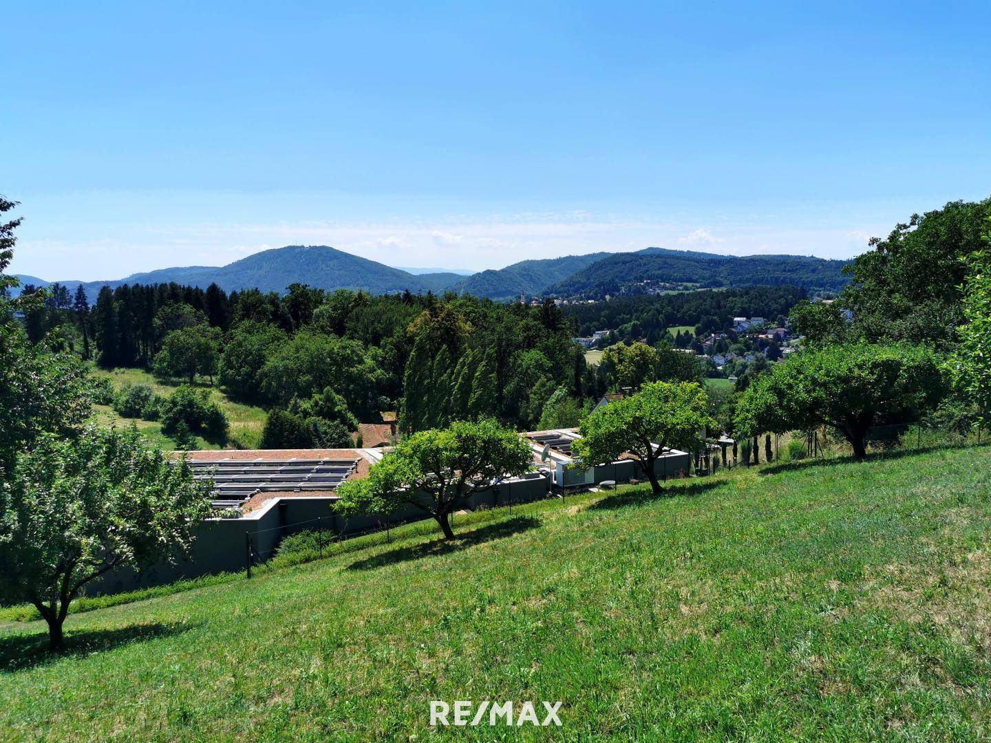 Panoramablick über ein großes, grünes Grundstück mit Bäumen und einer weiten Berglandschaft im Hintergrund.