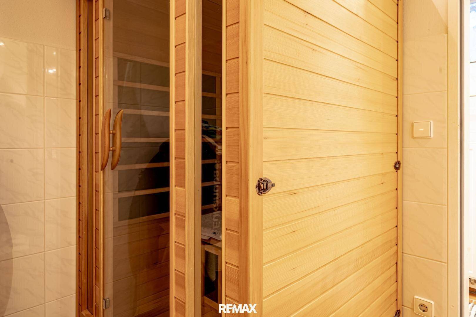 Moderne Holzsauna mit Glastür in einem gefliesten Raum, ideal zur Entspannung.