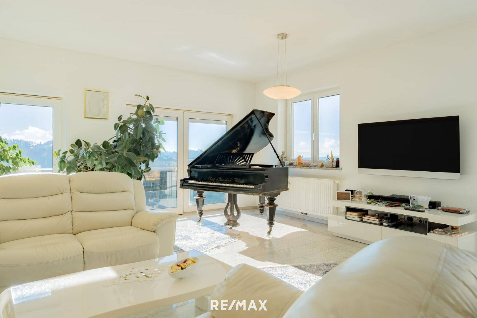 Helles Wohnzimmer mit elegantem Flügel, bequemen Sofas und Zugang zu einem sonnigen Außenbereich.