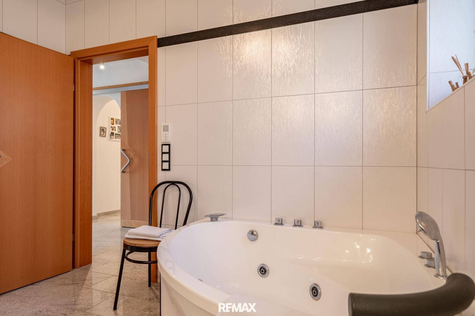 Geräumiges Badezimmer mit Whirlpool-Badewanne und weißen Fliesen, bereit zur Entspannung.
