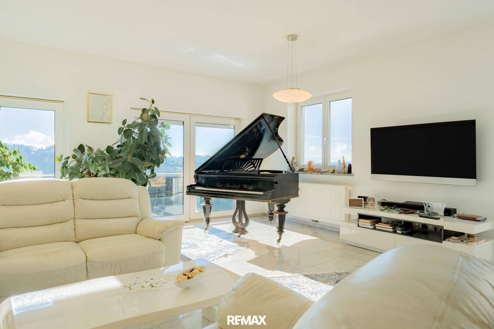 Helles Wohnzimmer mit großem Flügel, bequemen Sofas und Zugang zum Balkon.