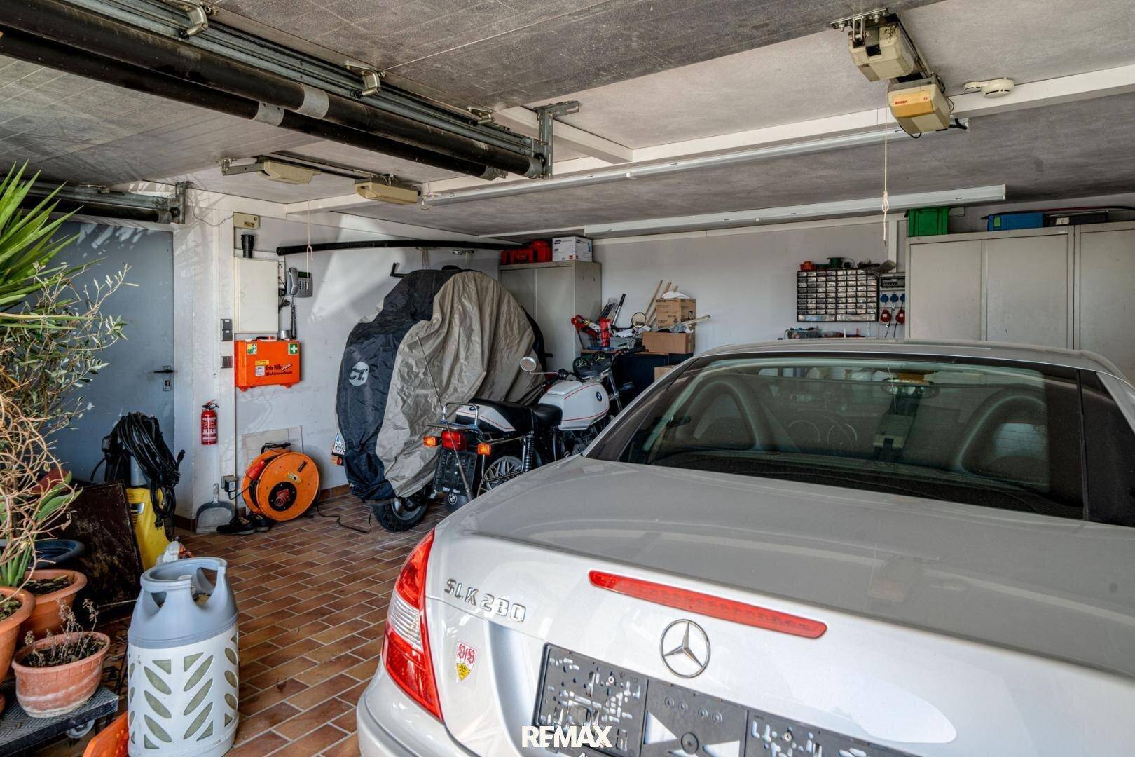 Geräumige Garage mit Platz für Fahrzeuge und zusätzlichem Stauraum, gefliester Boden.