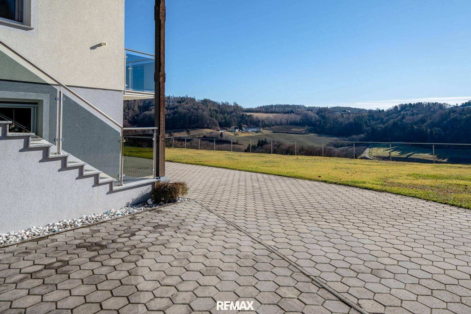 Außenansicht des Hauses mit gepflasterter Auffahrt und weitem Blick auf die grüne Landschaft.
