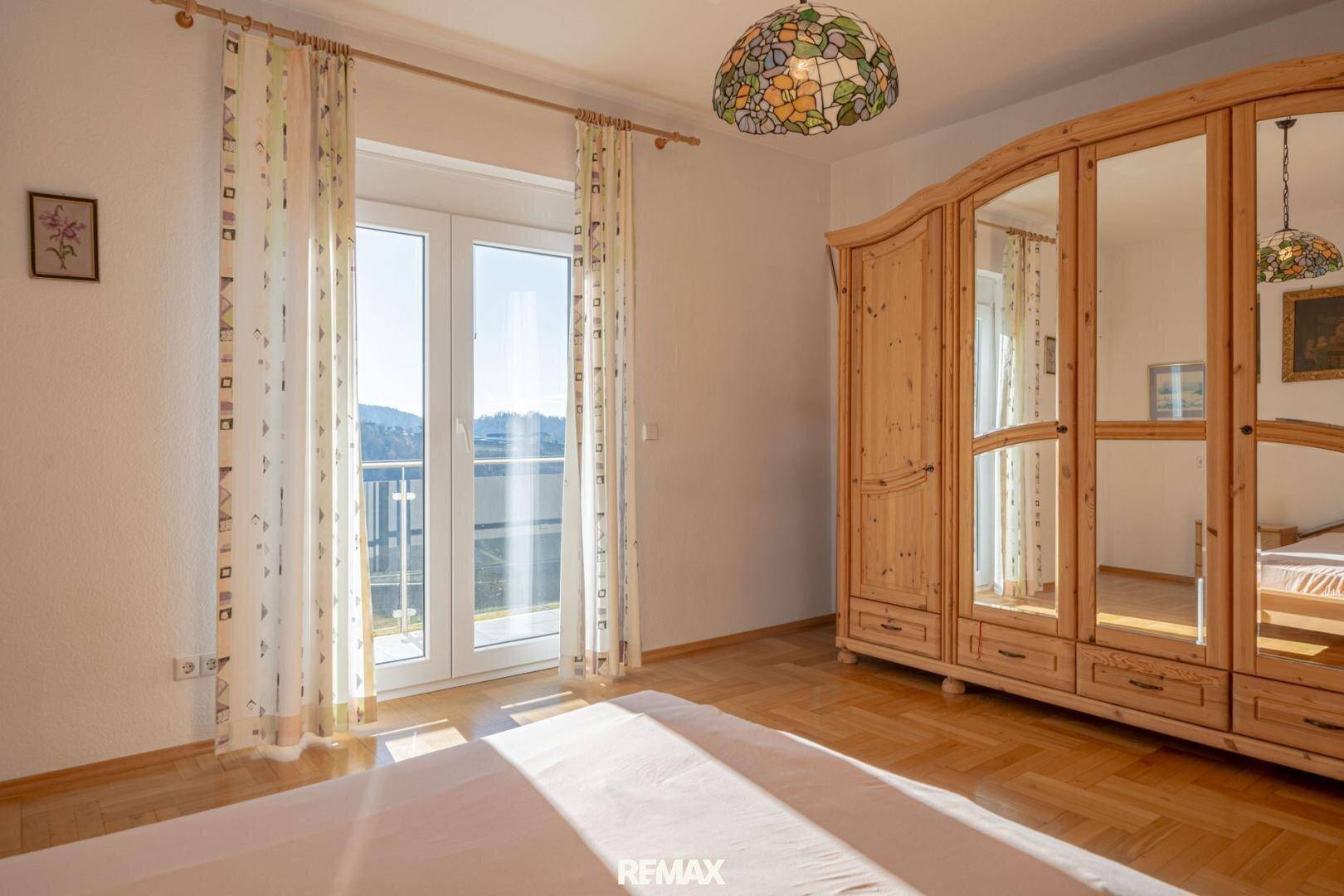 Schlafzimmer mit Holzkleiderschrank, Doppelbett und Zugang zum Balkon.