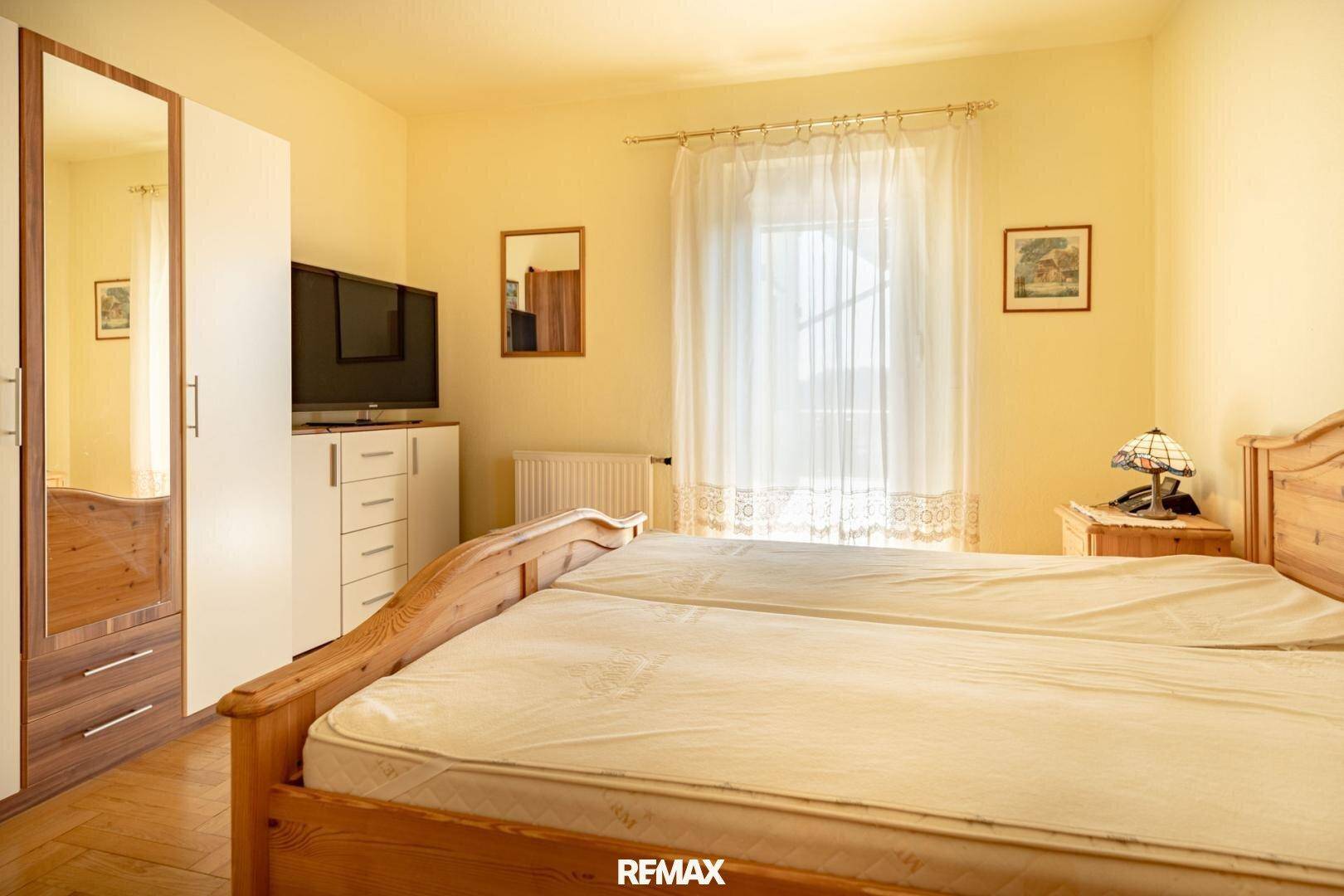 Helles Schlafzimmer mit Doppelbett, Holzmöbeln und großem Fenster.