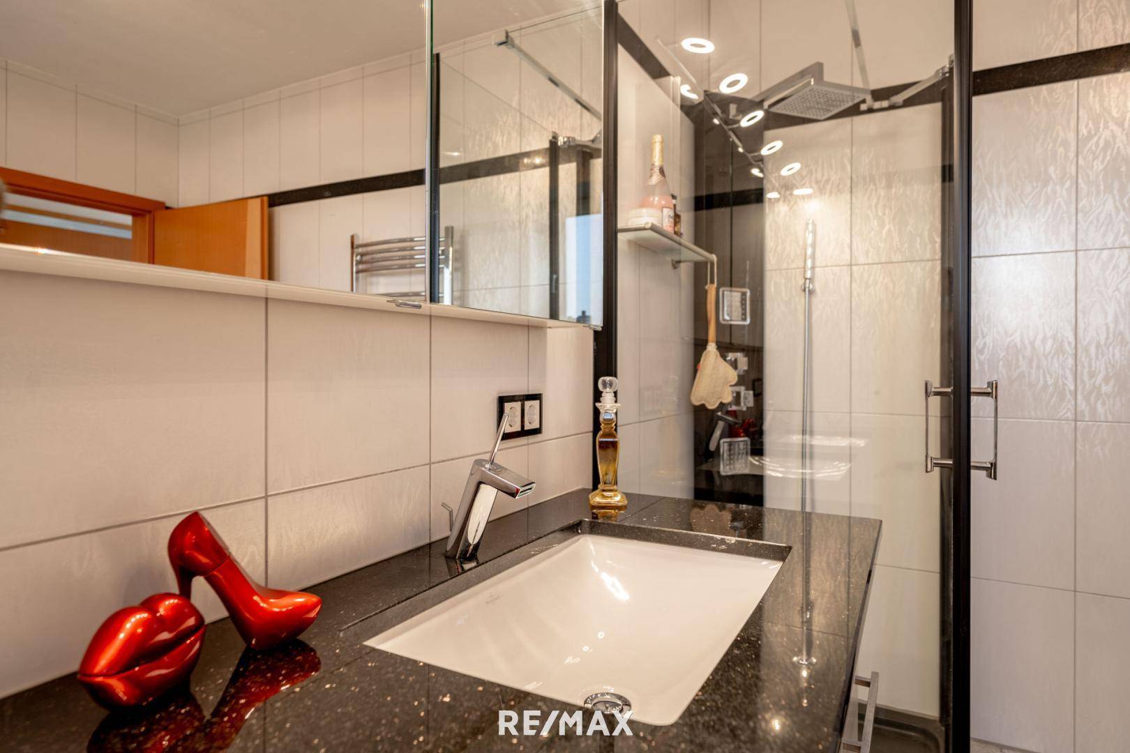 Modernes Badezimmer mit dunkler Granit-Arbeitsplatte, integriertem Waschbecken und Duschkabine.