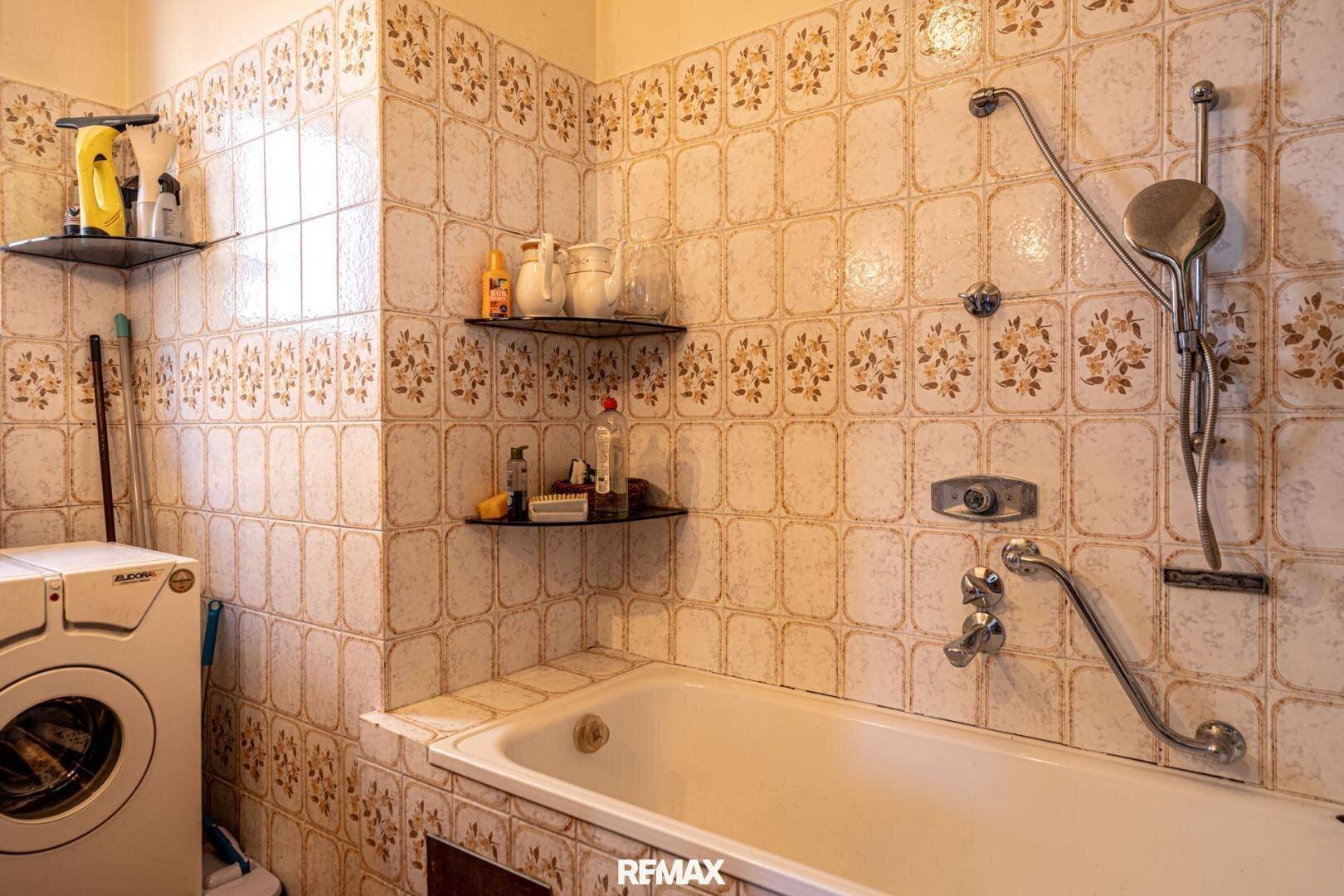 Badezimmer mit Badewanne, Dusche und Waschmaschine, gefliest im 80er-Jahre-Stil.