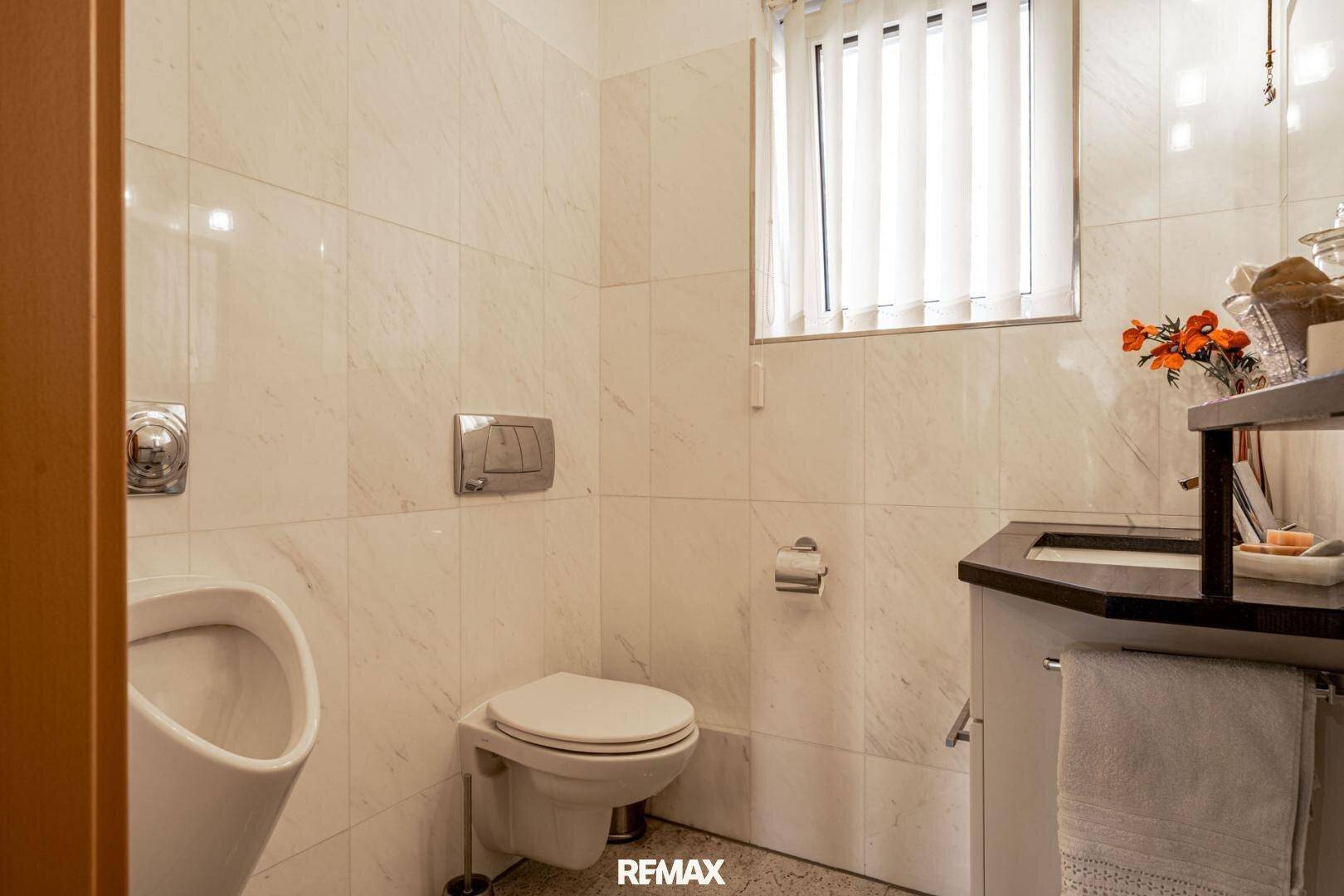 Separate Gästetoilette mit Urinal, Wand-WC und kleinem Waschbecken.
