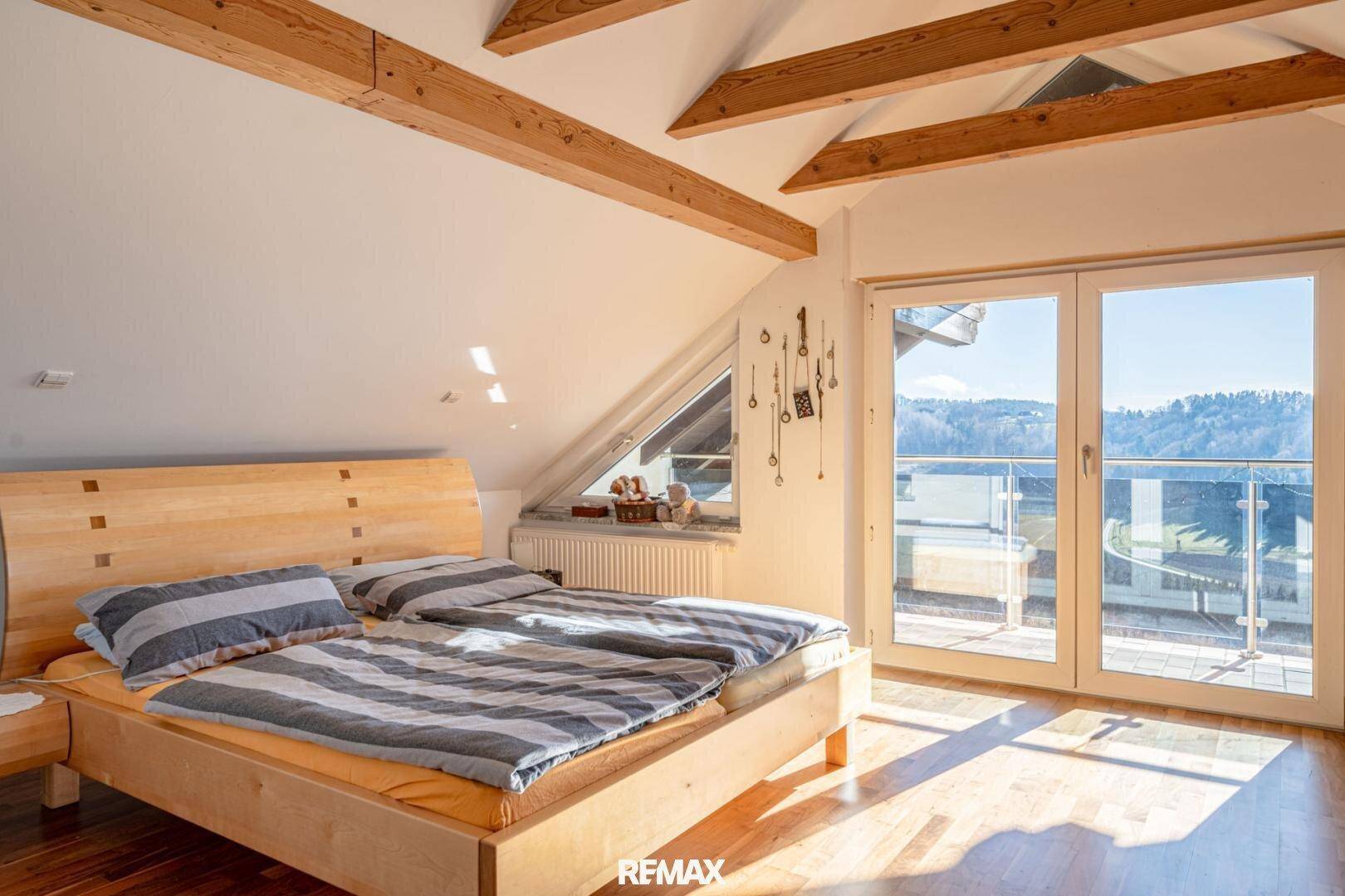 Helles Schlafzimmer im Dachgeschoss mit Holzbalken, Doppelbett und Balkonzugang.