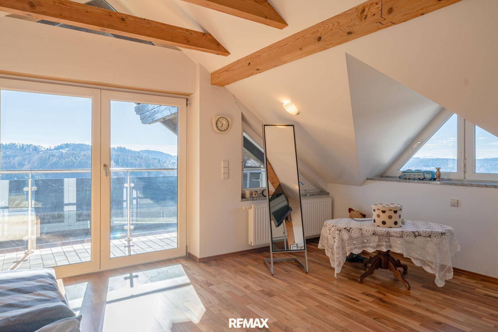 Dachgeschoss-Schlafzimmer mit Holzbalken, großem Spiegel und Zugang zum Balkon mit Aussicht.