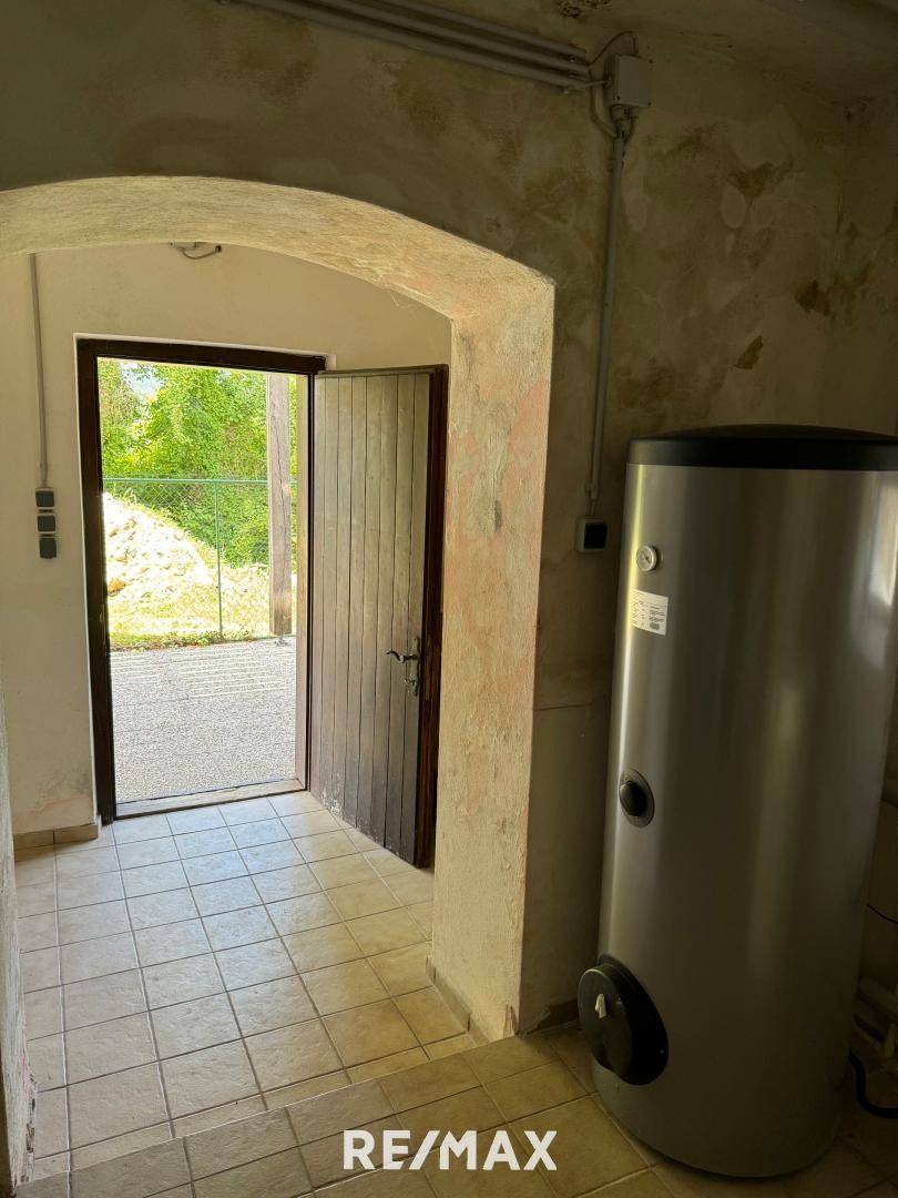 Eingangsbereich im Keller mit gefliestem Boden, Warmwasserspeicher und Zugang zum Außenbereich.