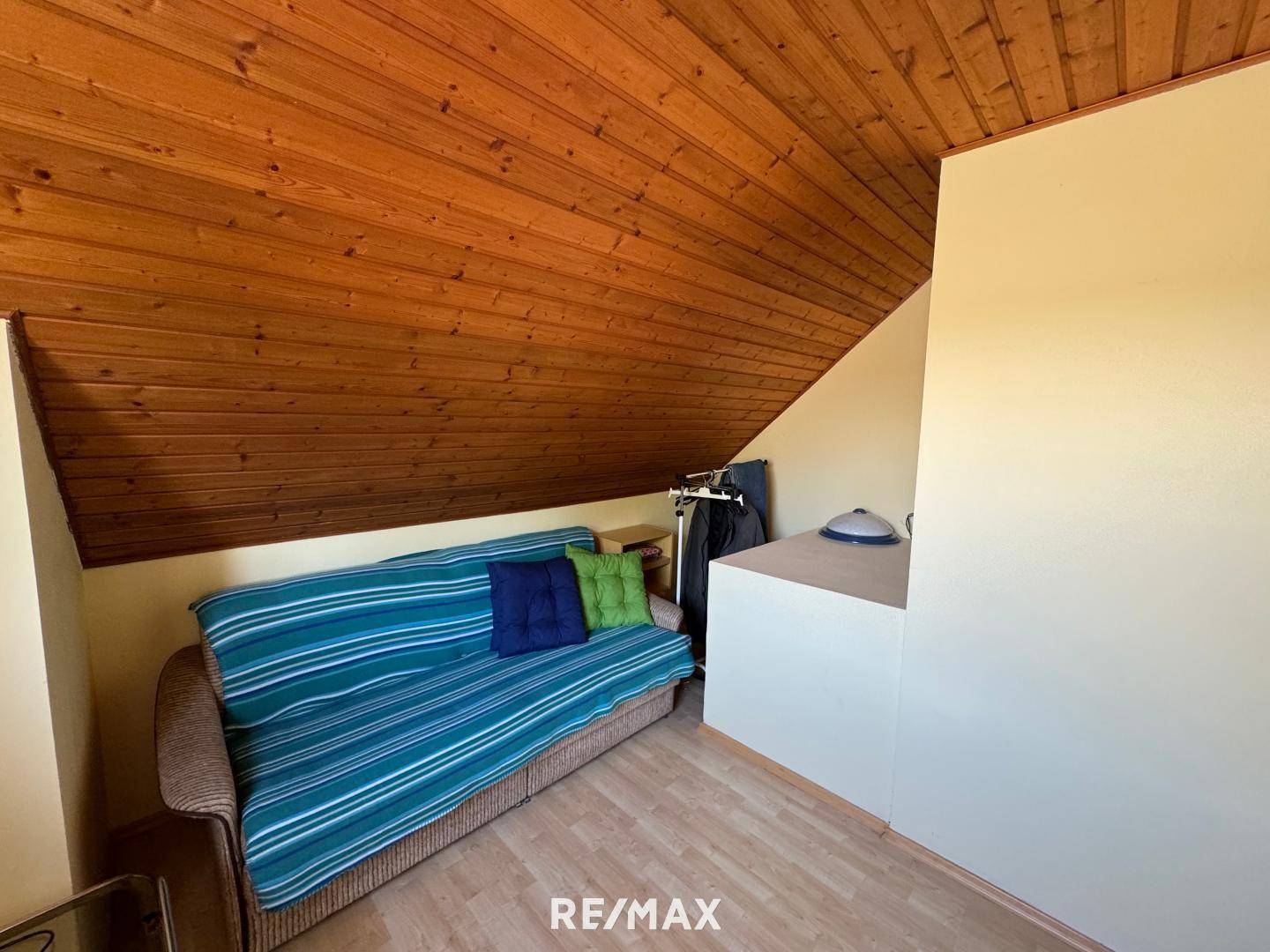 Zimmer mit Schlafsofa, Holzdachschräge und integriertem Stauraum, bietet praktische Nutzungsmöglichkeiten.