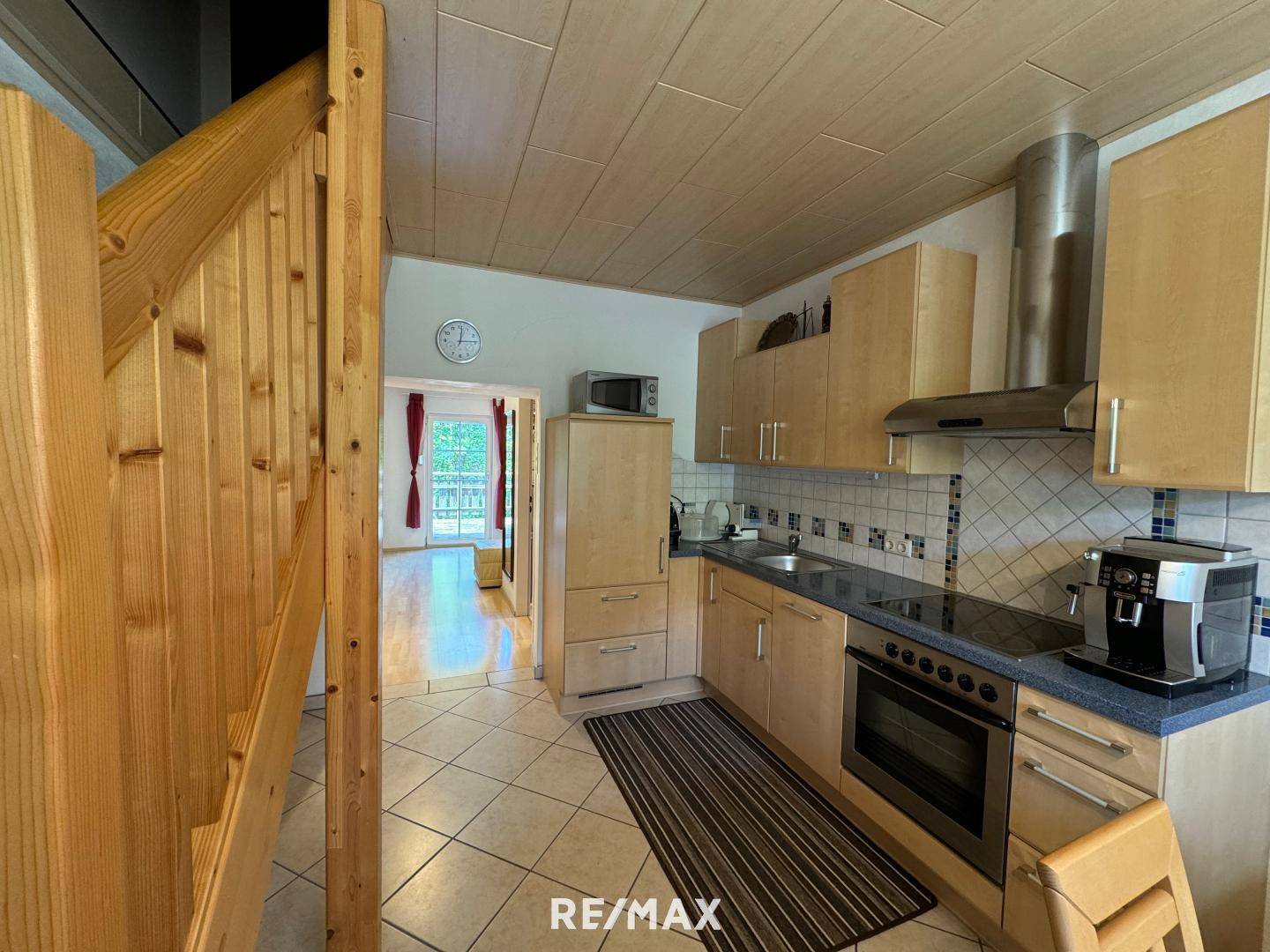 Funktionale Küche mit Holzschränken und Einbaugeräten, angrenzend an eine Holztreppe und einen weiteren Raum.